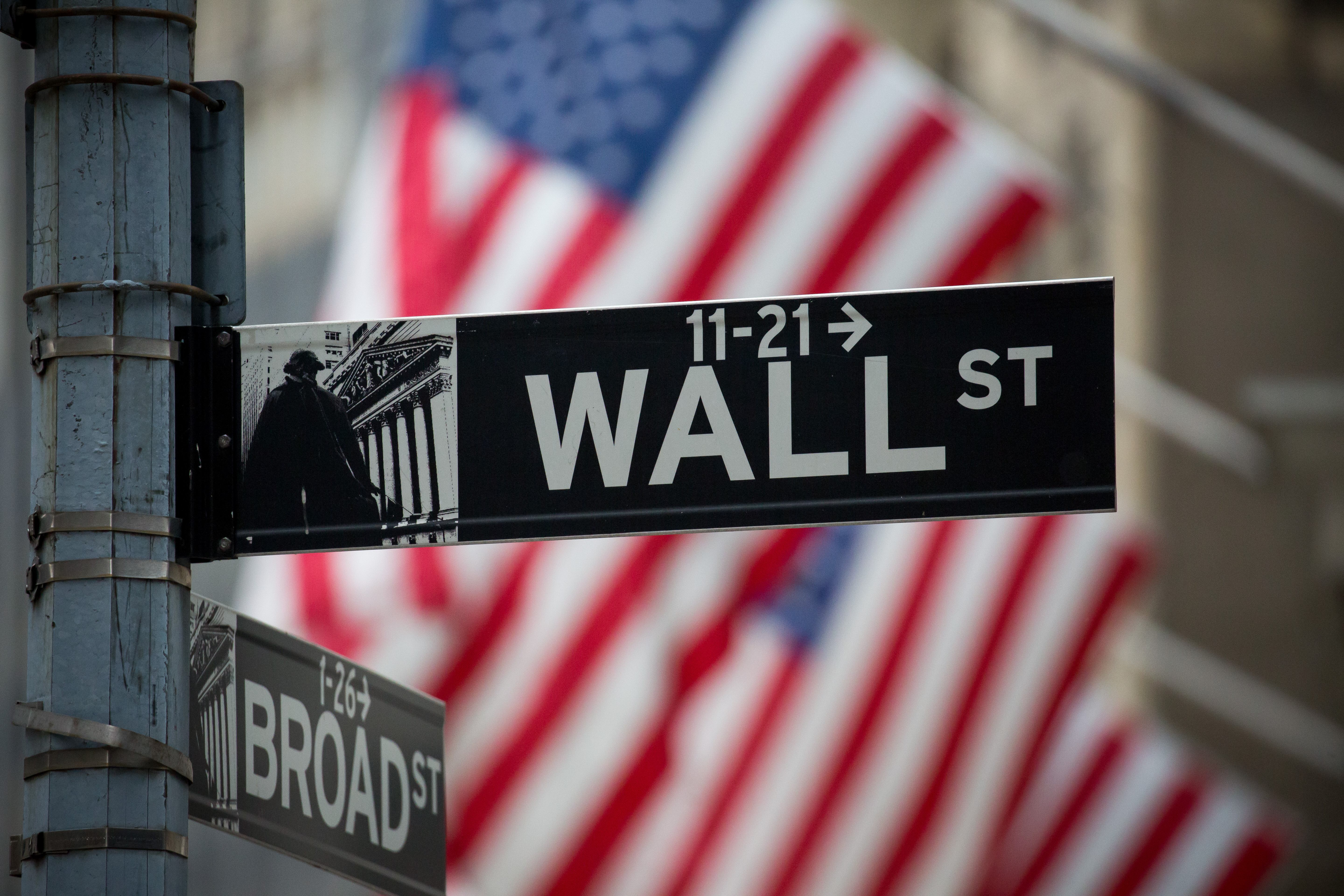A Wall Street sign is displayed as American flags fly in front of the New York Stock Exchange (NYSE) in New York, U.S., on Monday, Nov. 21, 2016.