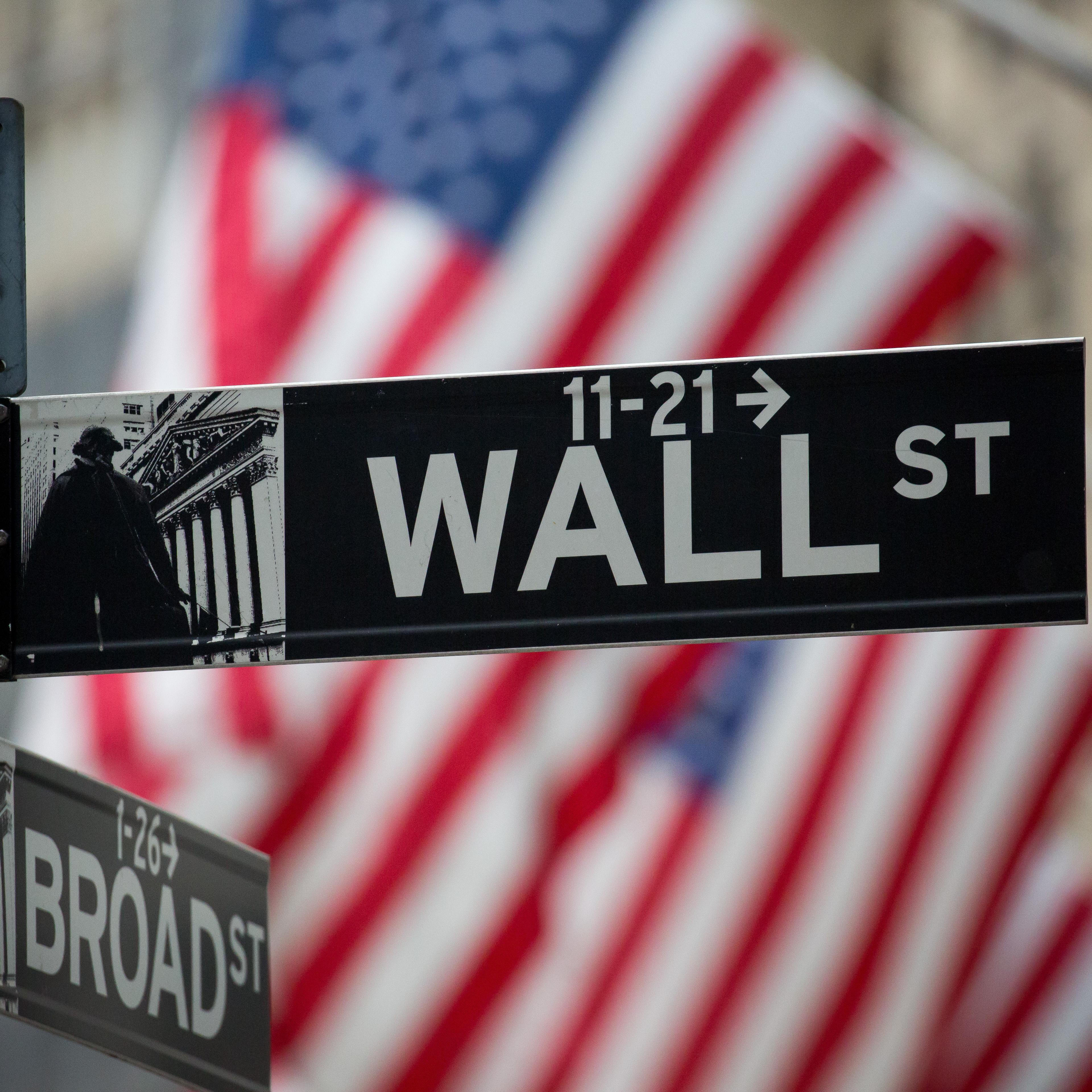 A Wall Street sign is displayed as American flags fly in front of the New York Stock Exchange (NYSE) in New York, U.S., on Monday, Nov. 21, 2016.