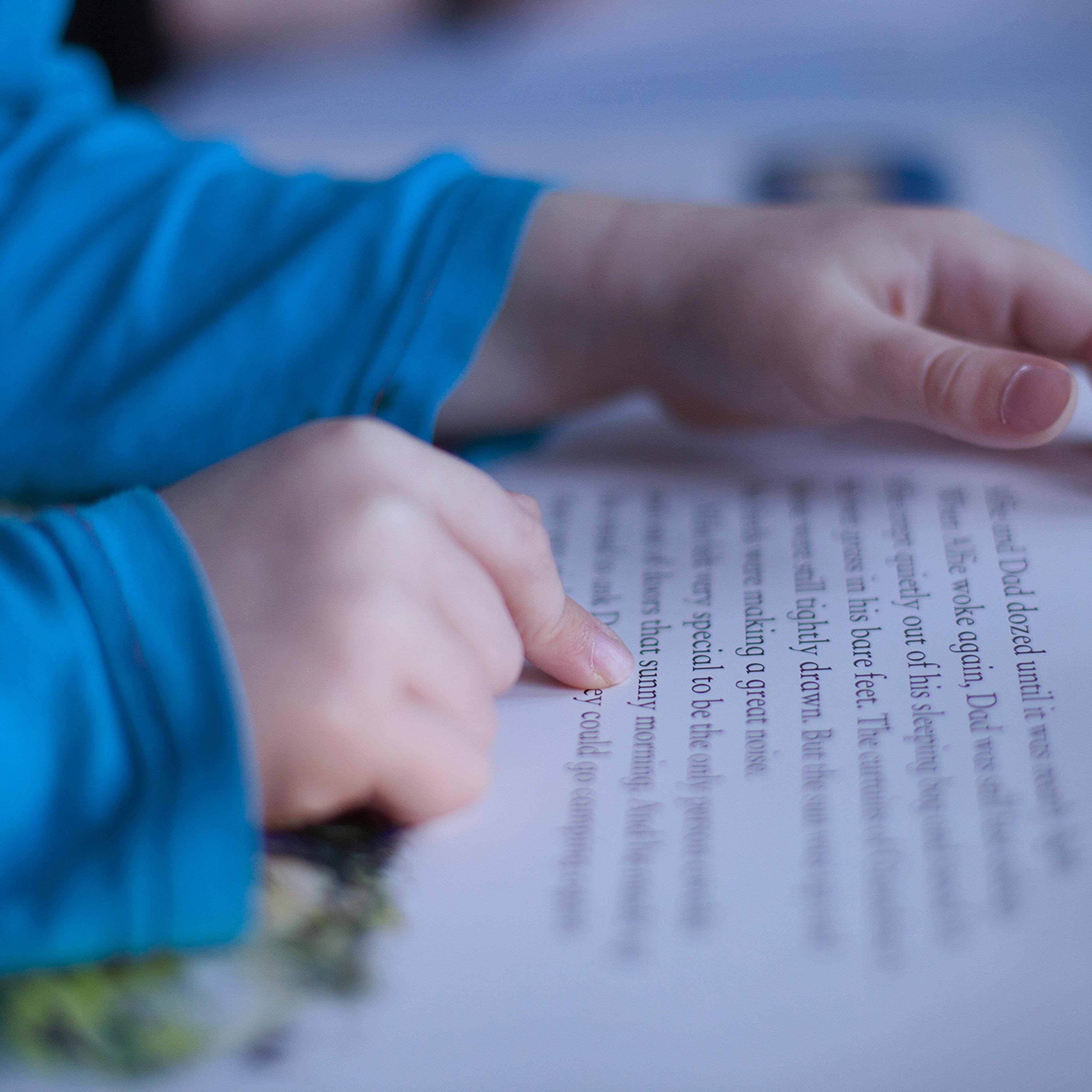 close up boys fingers pointing to words in book