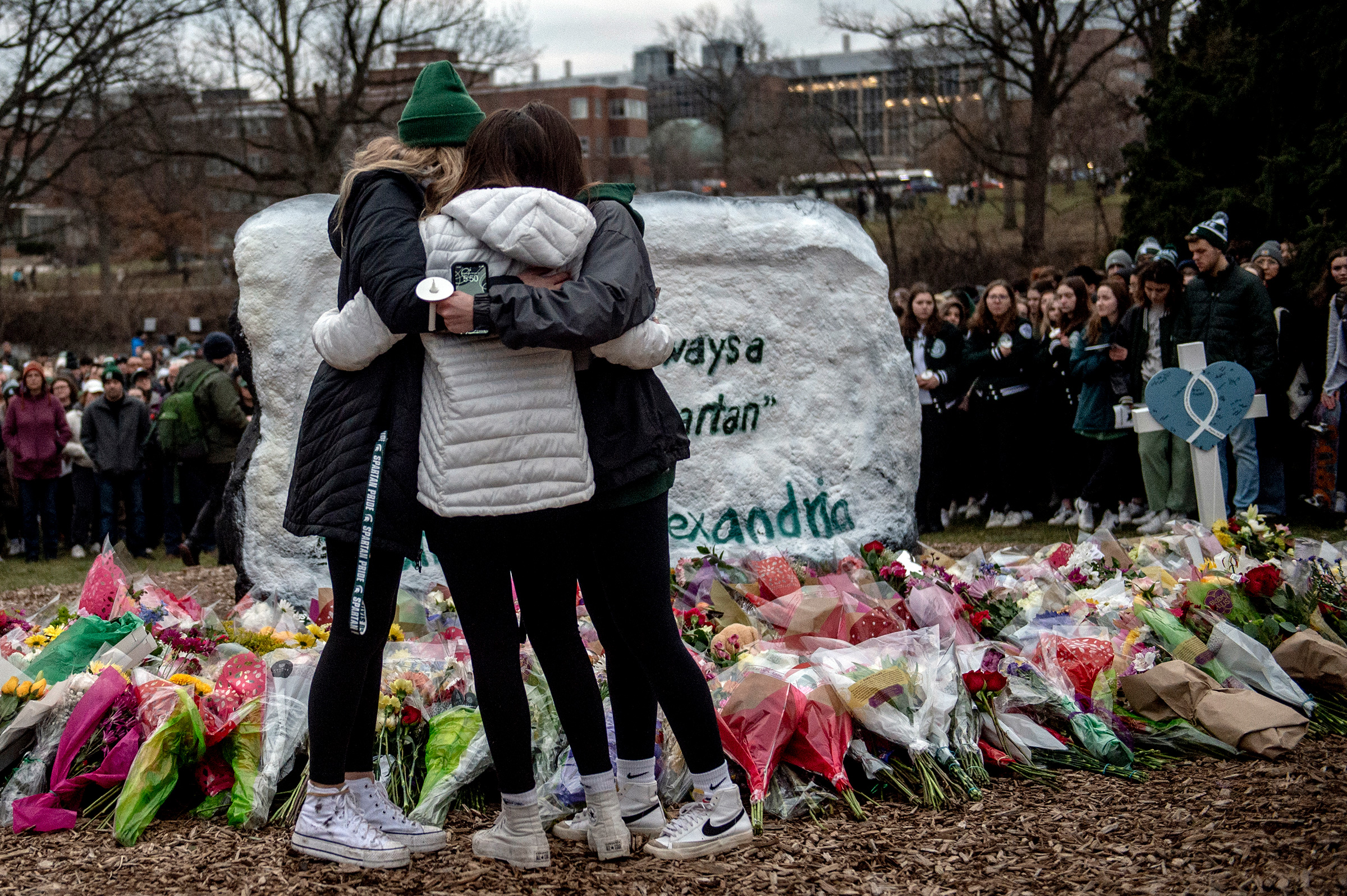 Michigan State freshman twins Lauren Schelling and Olivia Schelling, both 19, embrace their friend Brooke Goudreau, an 18-year-old MSU freshman from Southgate, while coping with the loss of three students at The Rock, a popular college landmark where a makeshift memorial continues to grow with flowers and keepsakes on Feb. 15 at Michigan State University in East Lansing, Mich. Two days ago on the evening of Feb. 13, three students were killed and others injured during a mass shooting on the campus. 