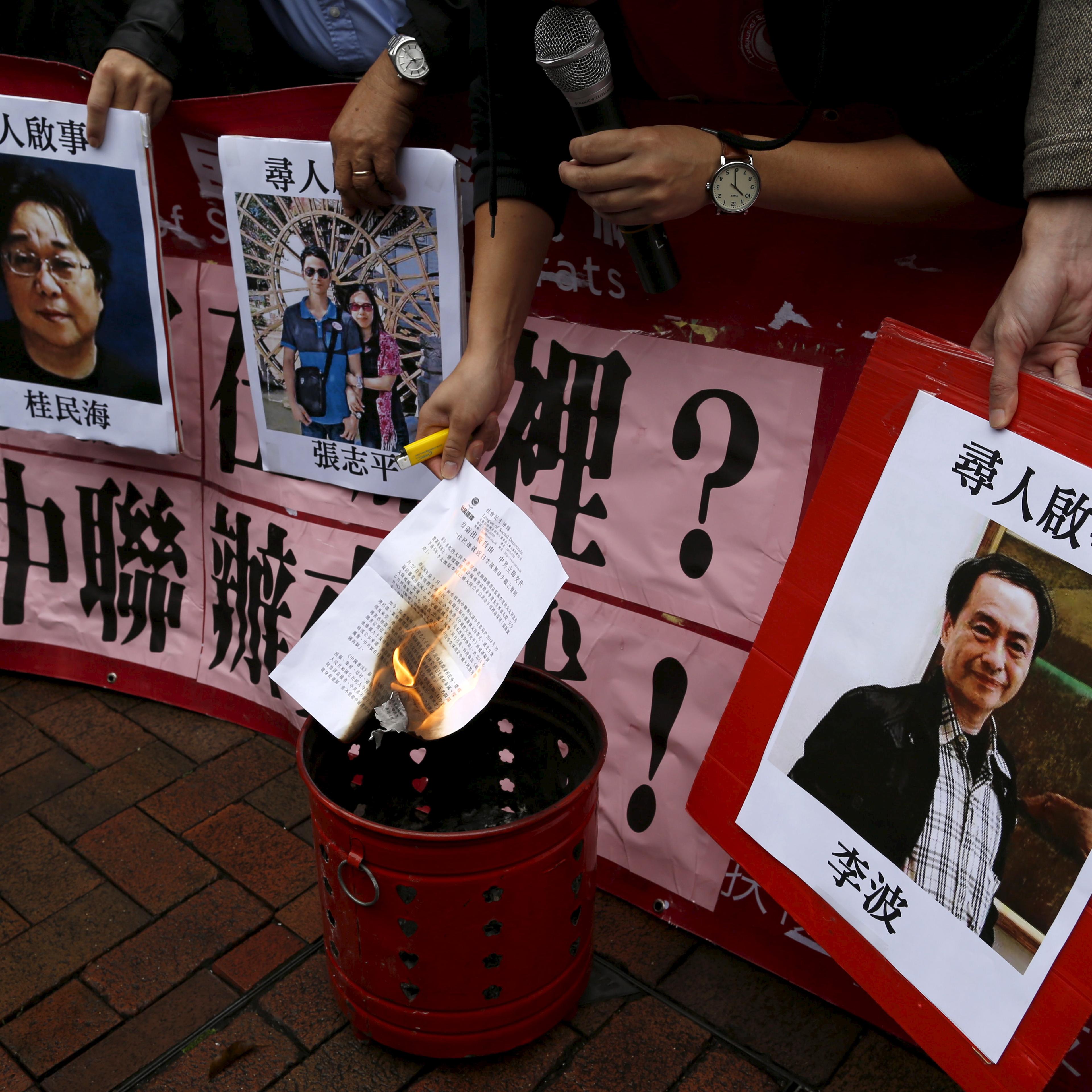 A pro-democracy demonstrator burns a letter next to pictures of missing staff members of a publishing house and a bookstore during a protest to call for an investigation behind their disappearance, outside the Chinese liaison office in Hong Kong