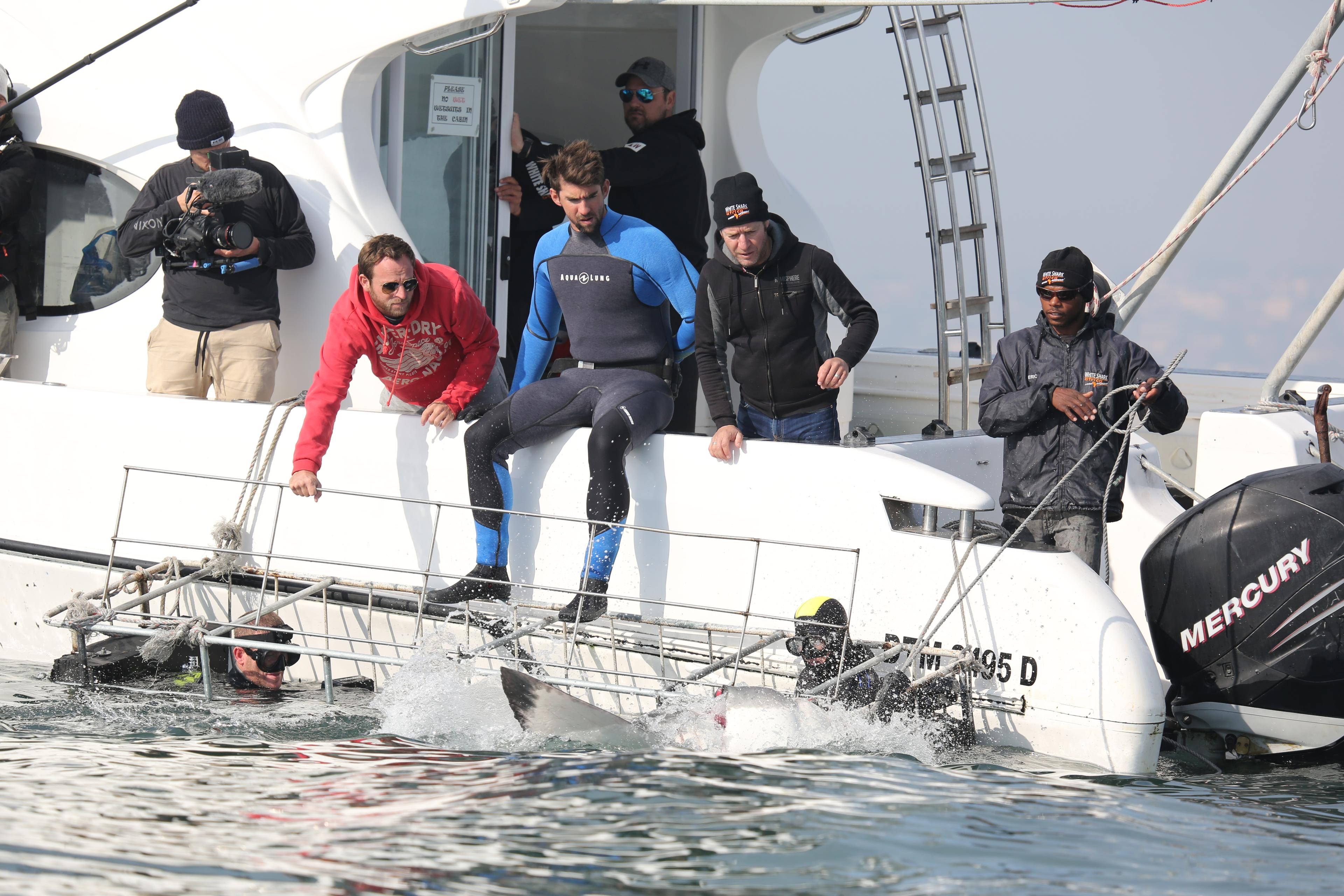 Phelps and the crew watch a shark approach the cage, which Michael is about to enter.