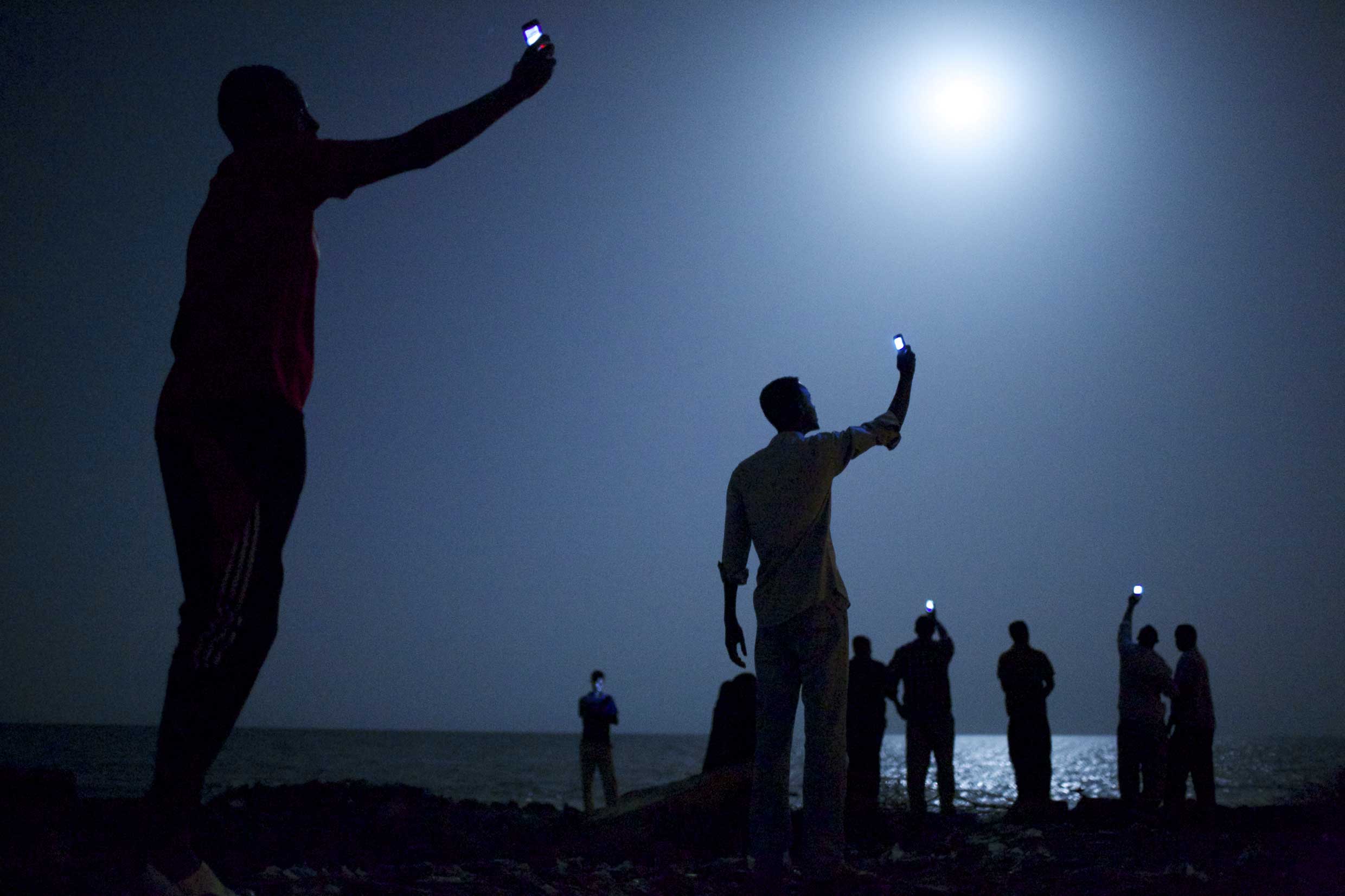 World Press Photo of the Year 2013.26 February 2013, Djibouti City, Djibouti. African migrants on the shore of Djibouti city at night, raising their phones in an attempt to capture an inexpensive signal from neighboring SomaliaÑa tenuous link to relative