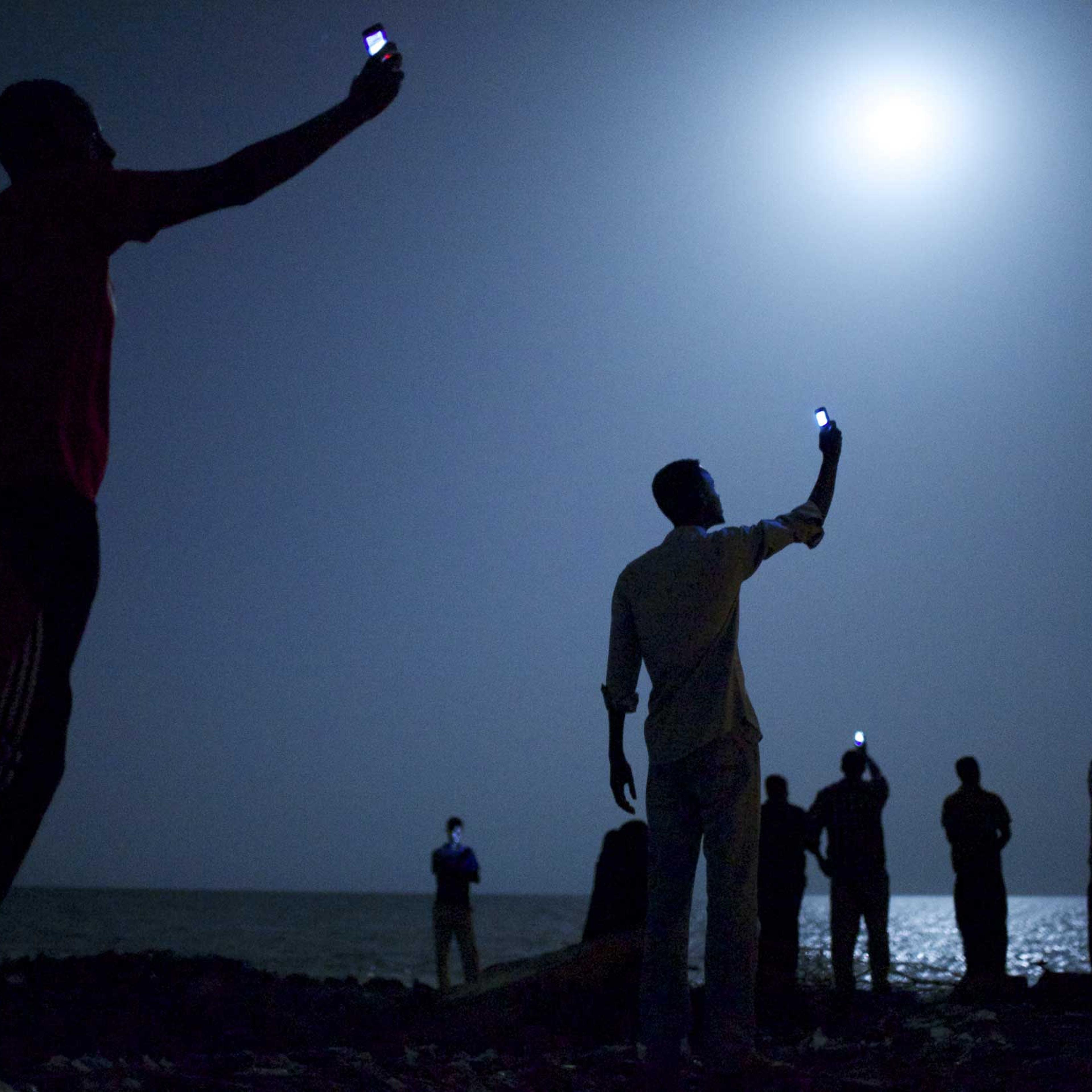 World Press Photo of the Year 2013.26 February 2013, Djibouti City, Djibouti. African migrants on the shore of Djibouti city at night, raising their phones in an attempt to capture an inexpensive signal from neighboring SomaliaÑa tenuous link to relative