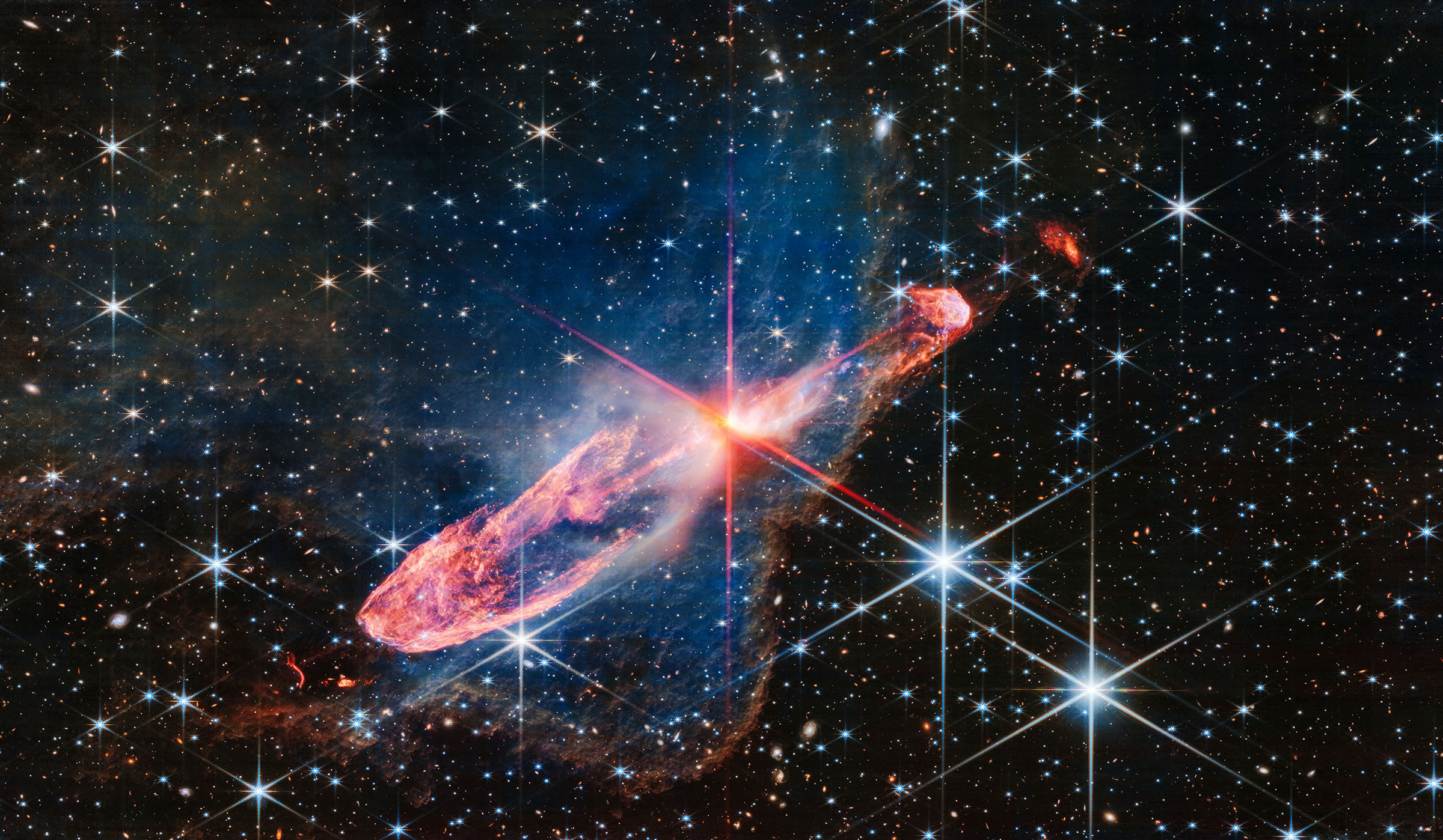 At the center of the image is a horizontal orange cloud known as Herbig-Haro 46/47 that is uneven with rounded ends, and tilted from bottom left to top right. In the middle of this cloud is a yellow-white blob with 8 reddish pink diffraction spikes pierc