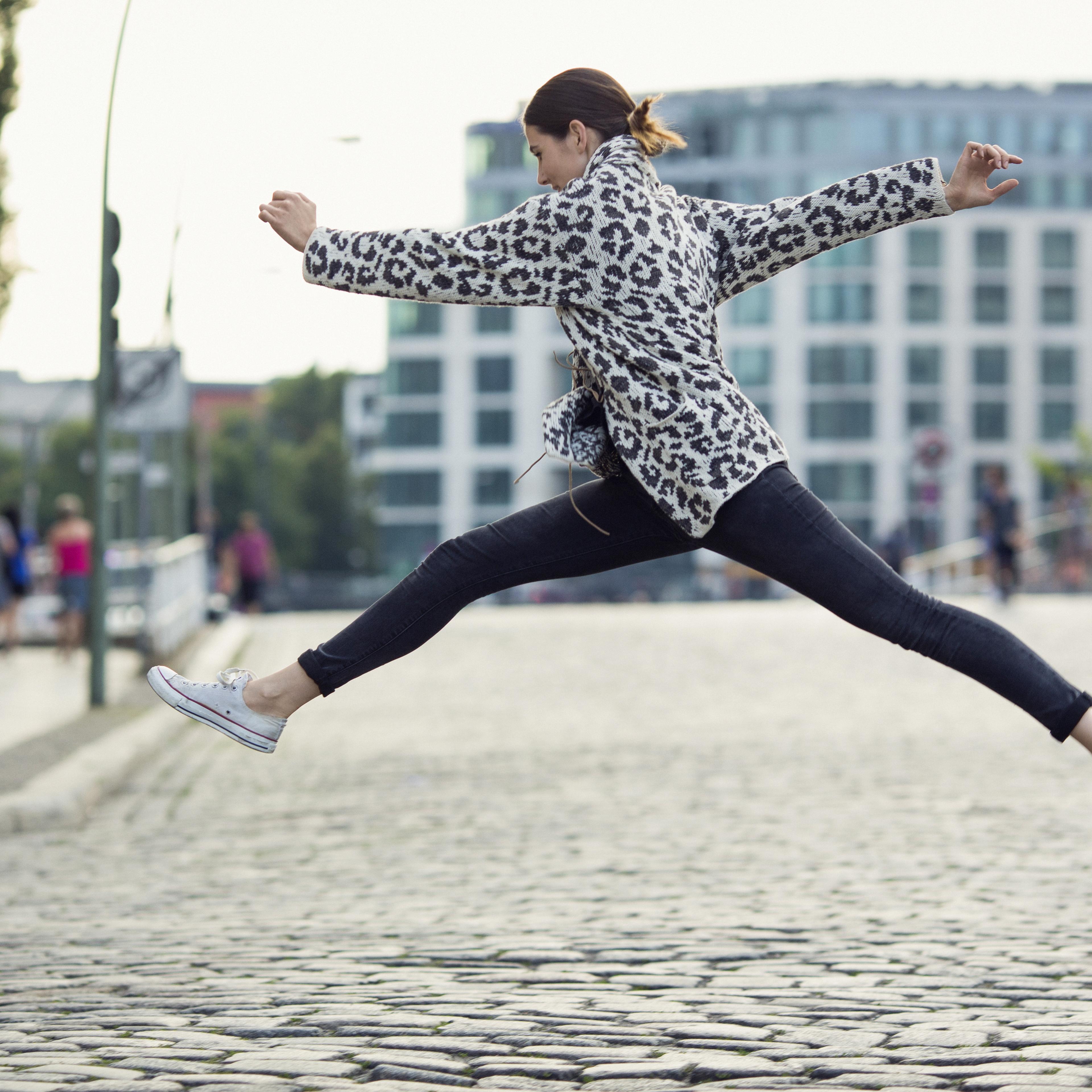 woman making a big jump in a sunny city street