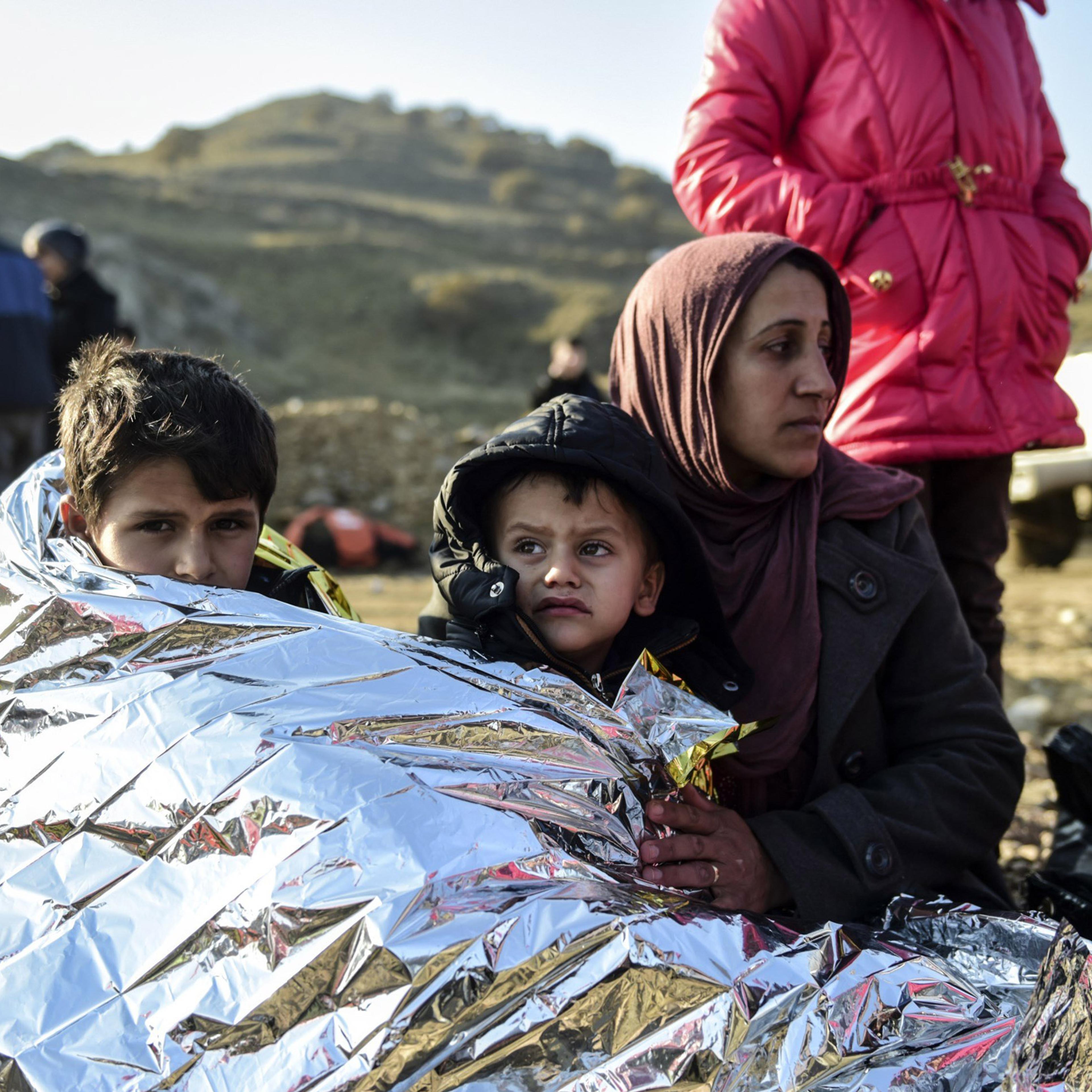 A Syrian family waits after arriving on the Greek island of Lesbos along with other migrants and refugees, on November 17, 2015, after crossing the Aegean Sea from Turkey. At least eight people drowned when a boat carrying migrants from Turkey sank off t