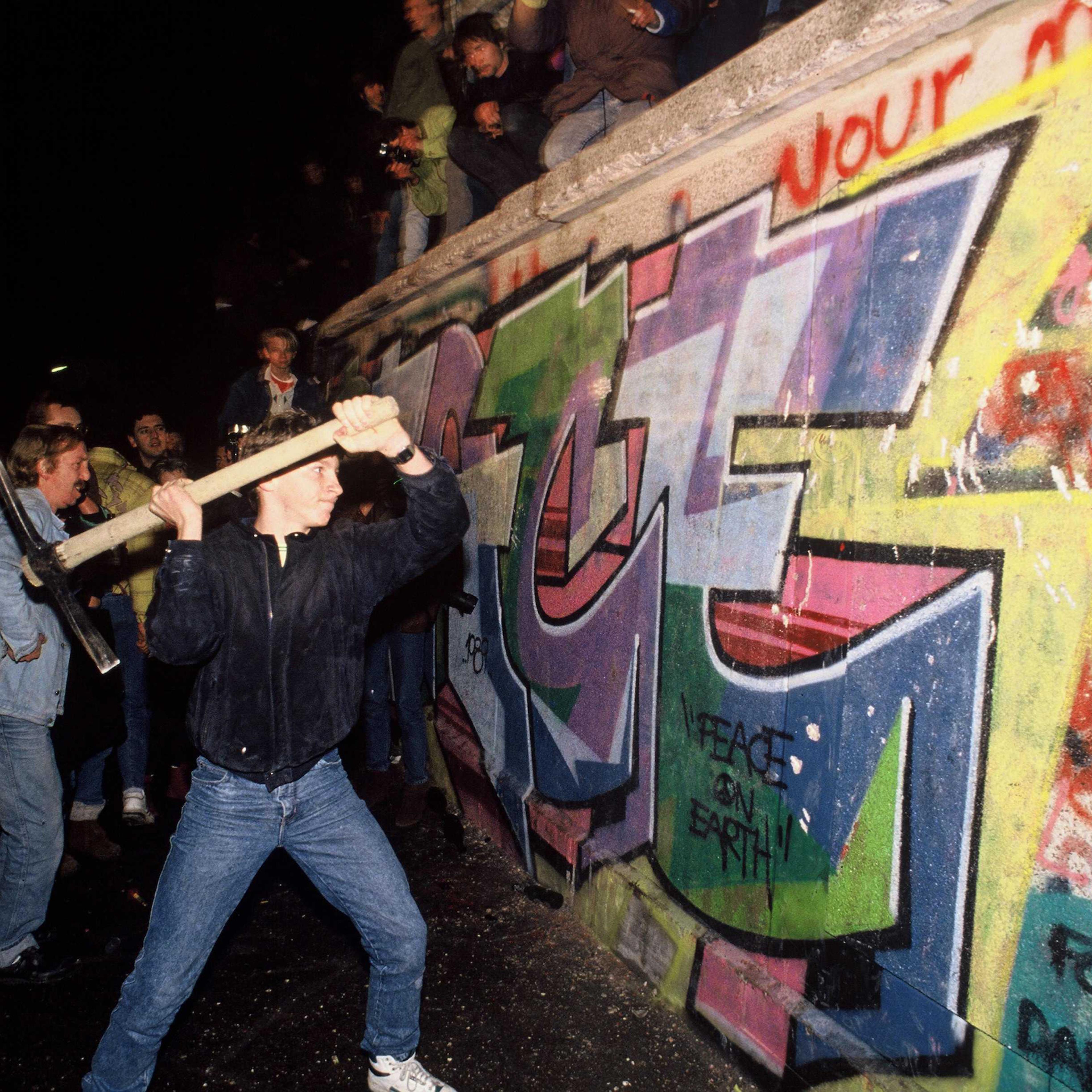 A man attacks the Berlin Wall with a pickaxe on the night of November 9th, 1989