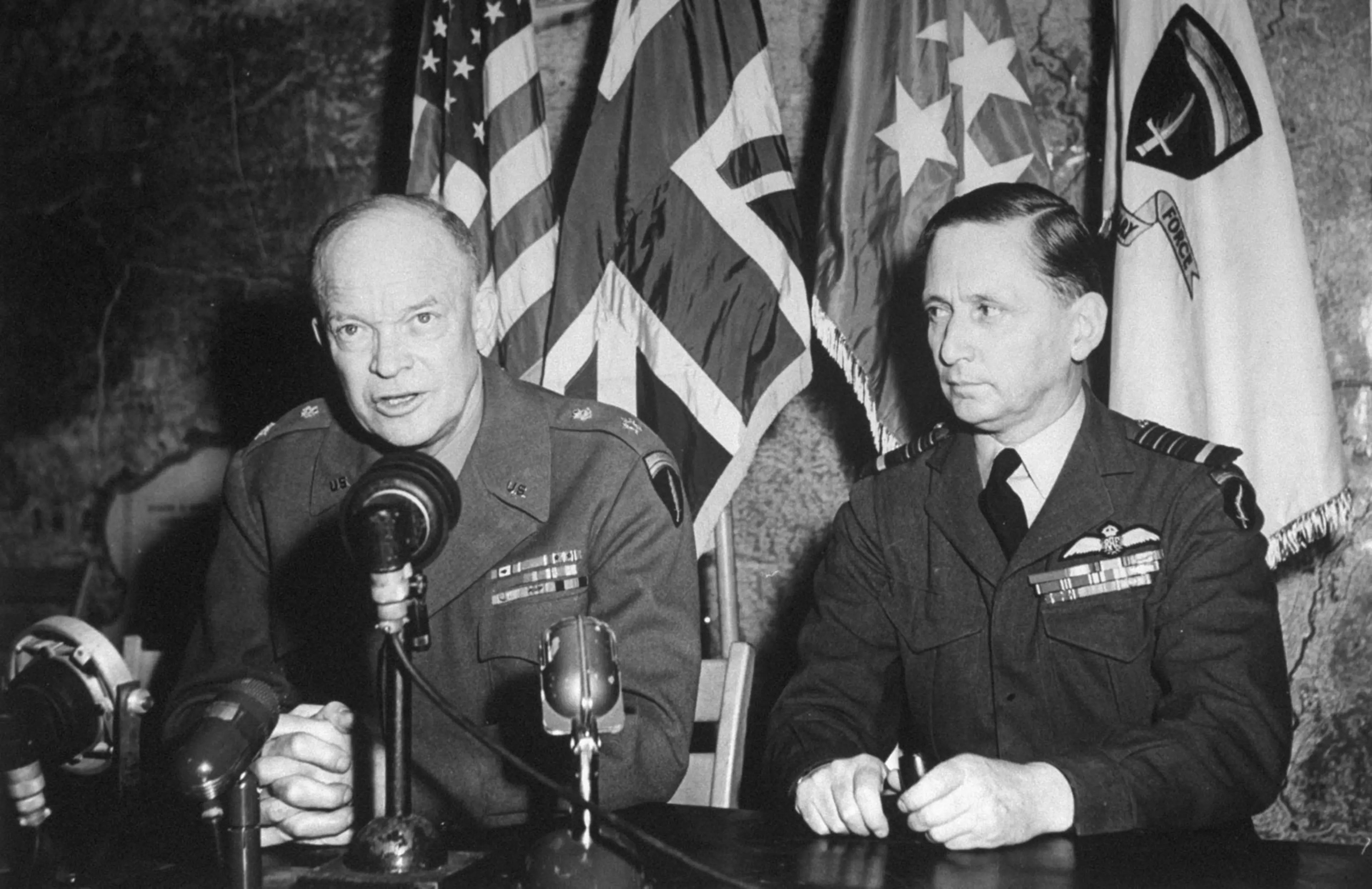 In surrender room Eisenhower makes victory speech. Behind are flags of U.S., Britain. Eisenhower (five stars) and SHAEF. Eisenhower's biggest job had been done magnificently.