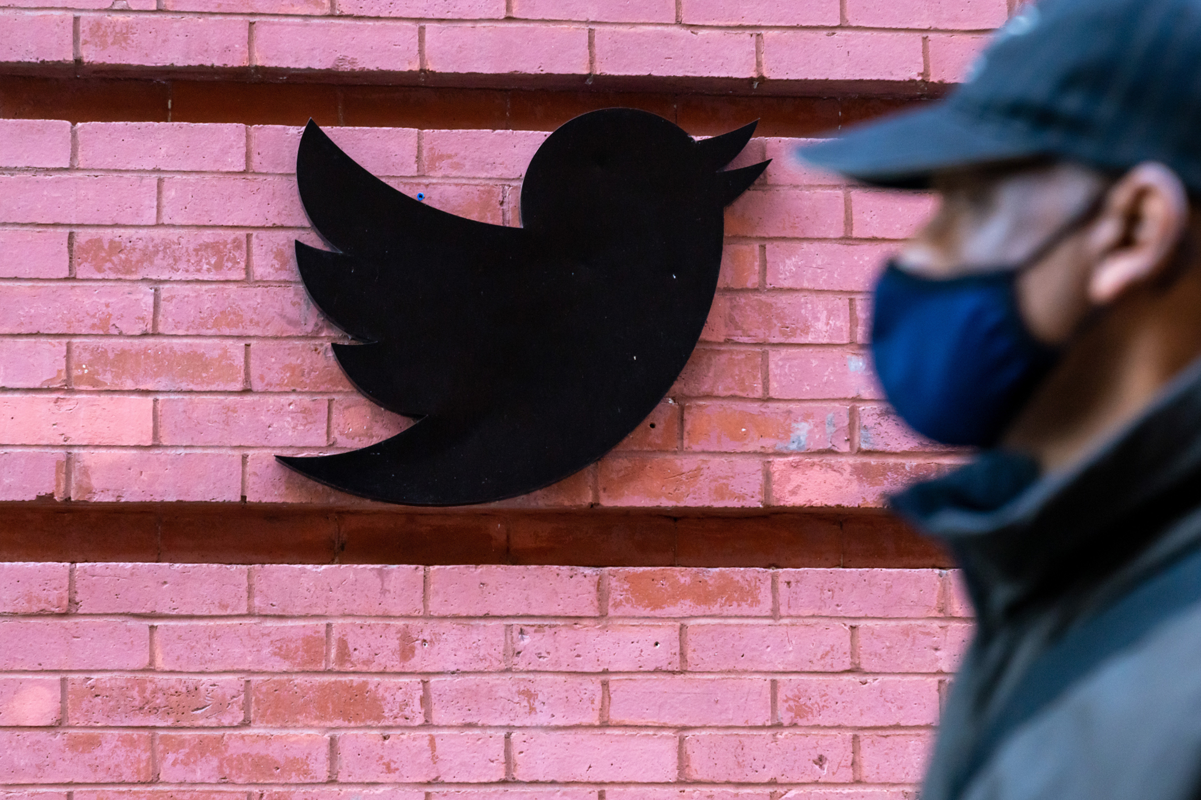 A man wearing a face mask walks past a Twitter logo outside