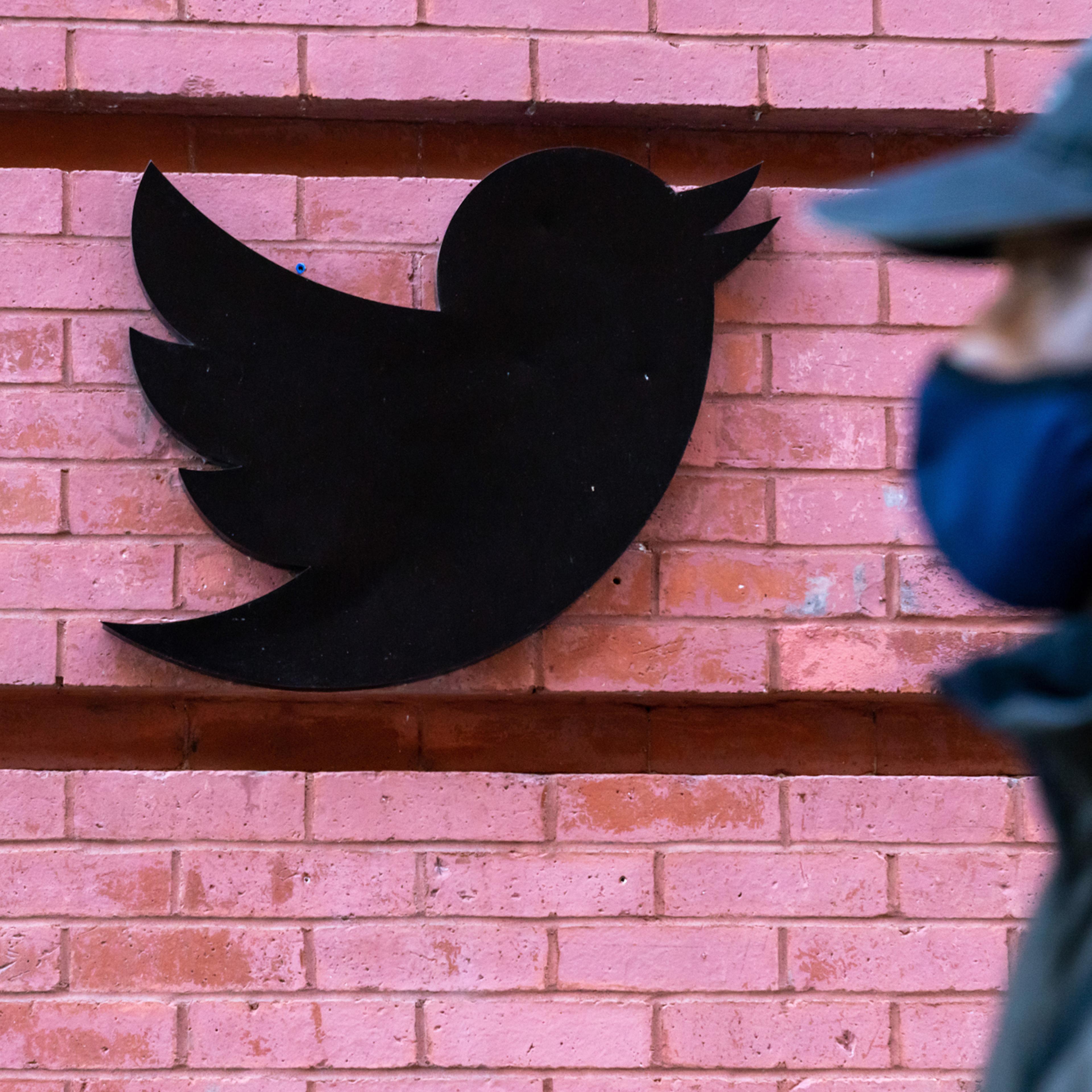 A man wearing a face mask walks past a Twitter logo outside