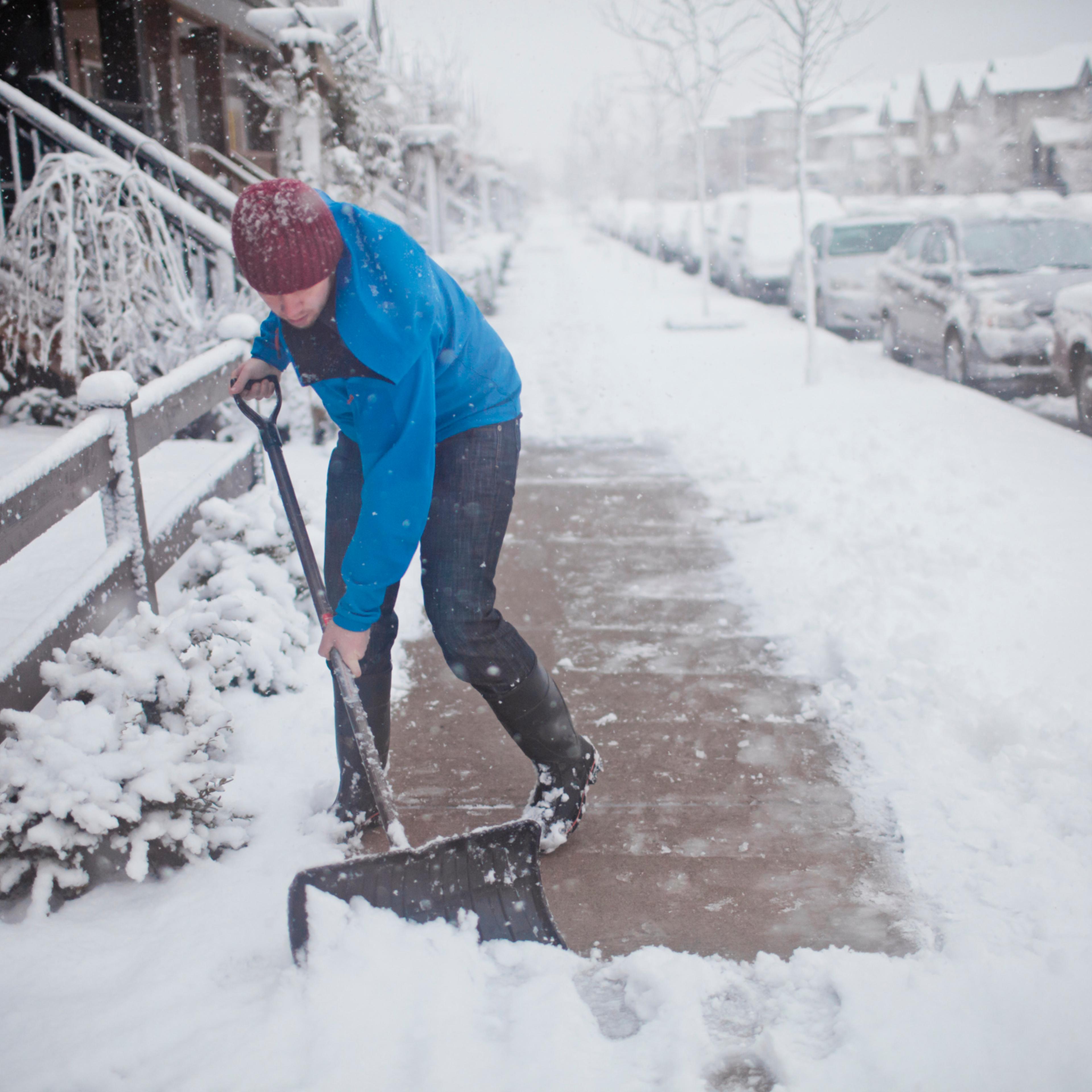 A man shovels the sidewalk outside of his suburban house.
