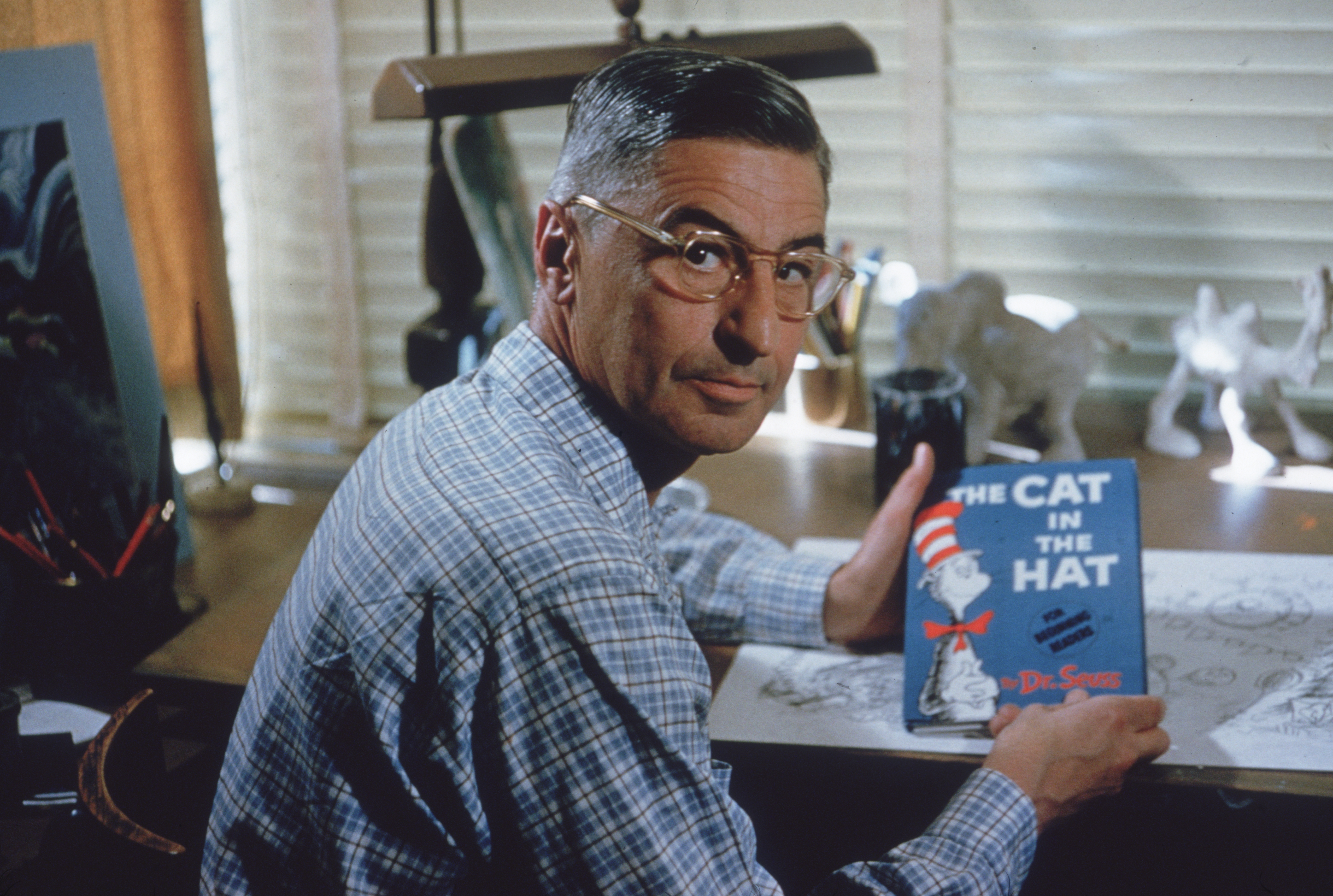 American author and illustrator Dr Seuss (Theodor Seuss Geisel, 1904 - 1991) sits at his drafting table in his home office with a copy of his book, 'The Cat in the Hat', La Jolla, California, April 25, 1957.
