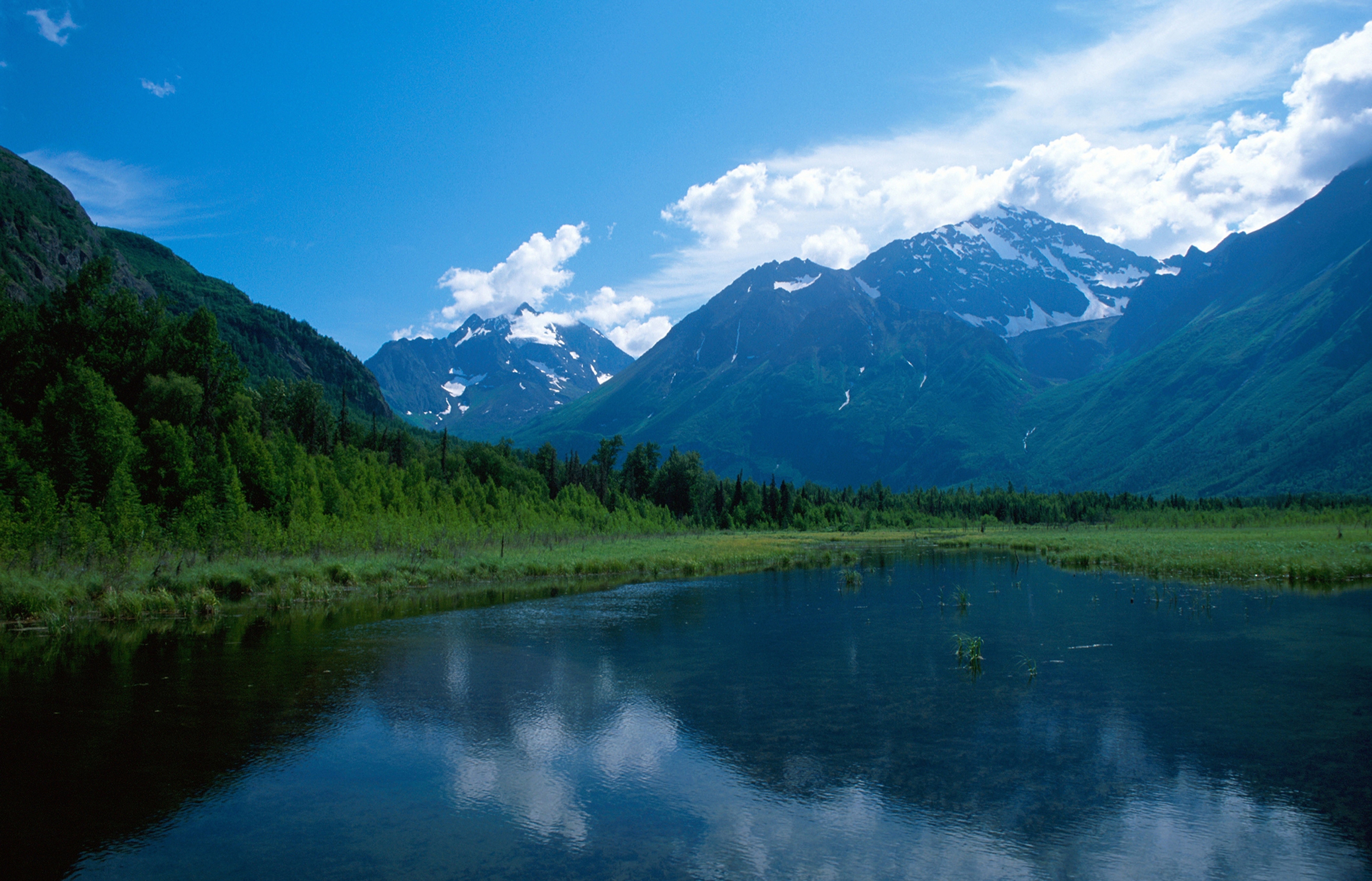 Snow covers portions of Alaskan mountain range in the distance, as seen from across a small body of water, 2014.
