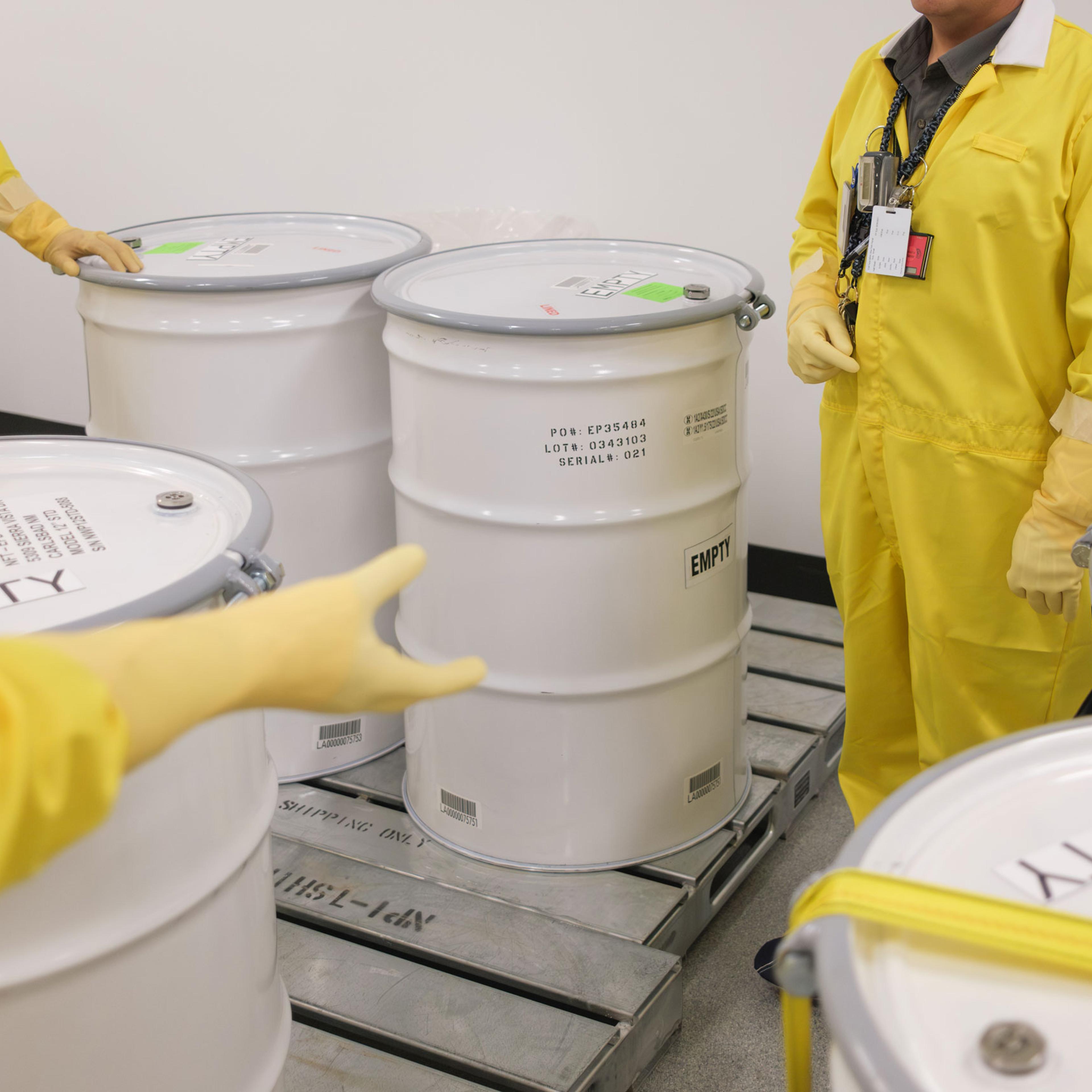 lab employees wearing yellow suits stand by empty waste drums used for training