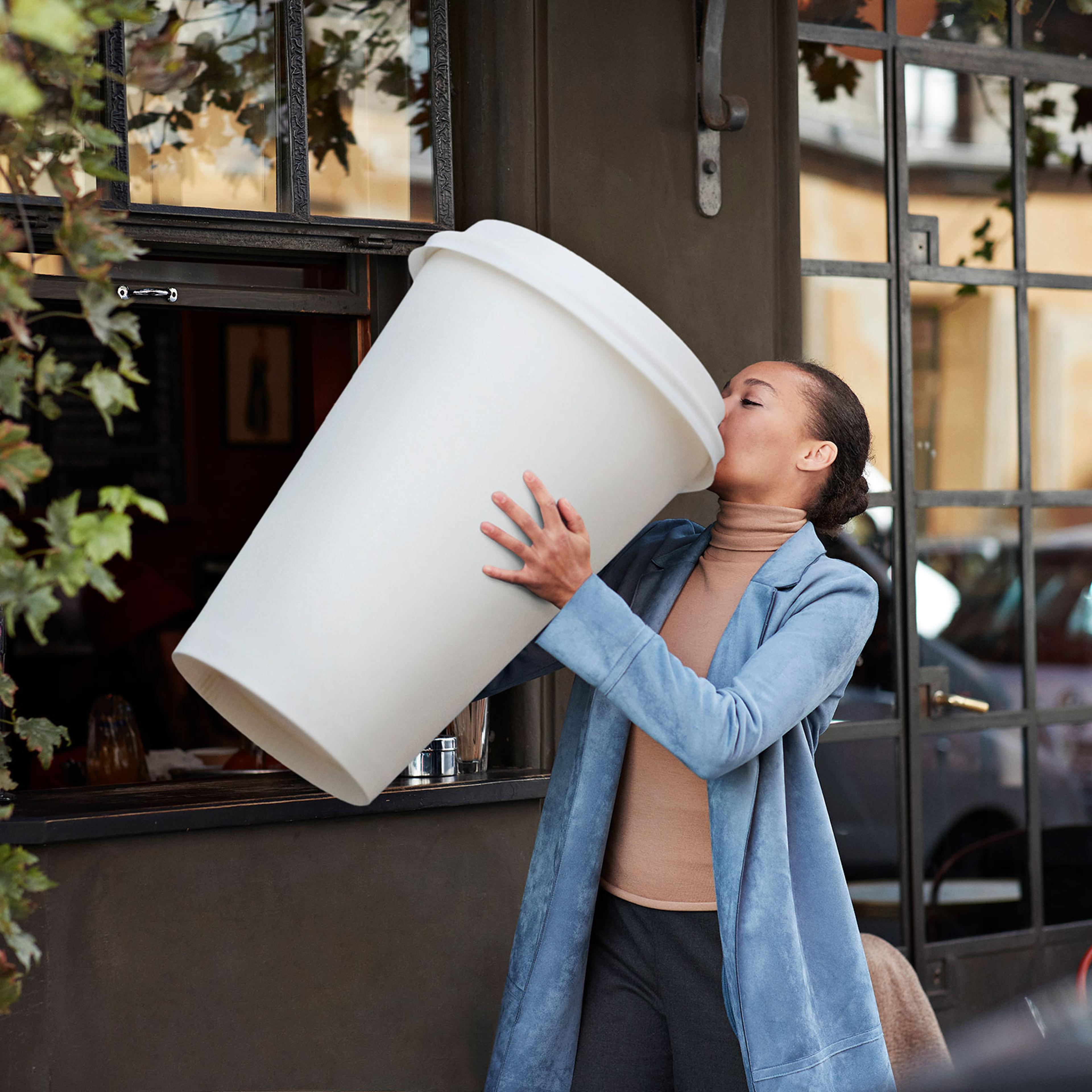 Woman drinking coffee from large disposable cup at take away counter of cafe