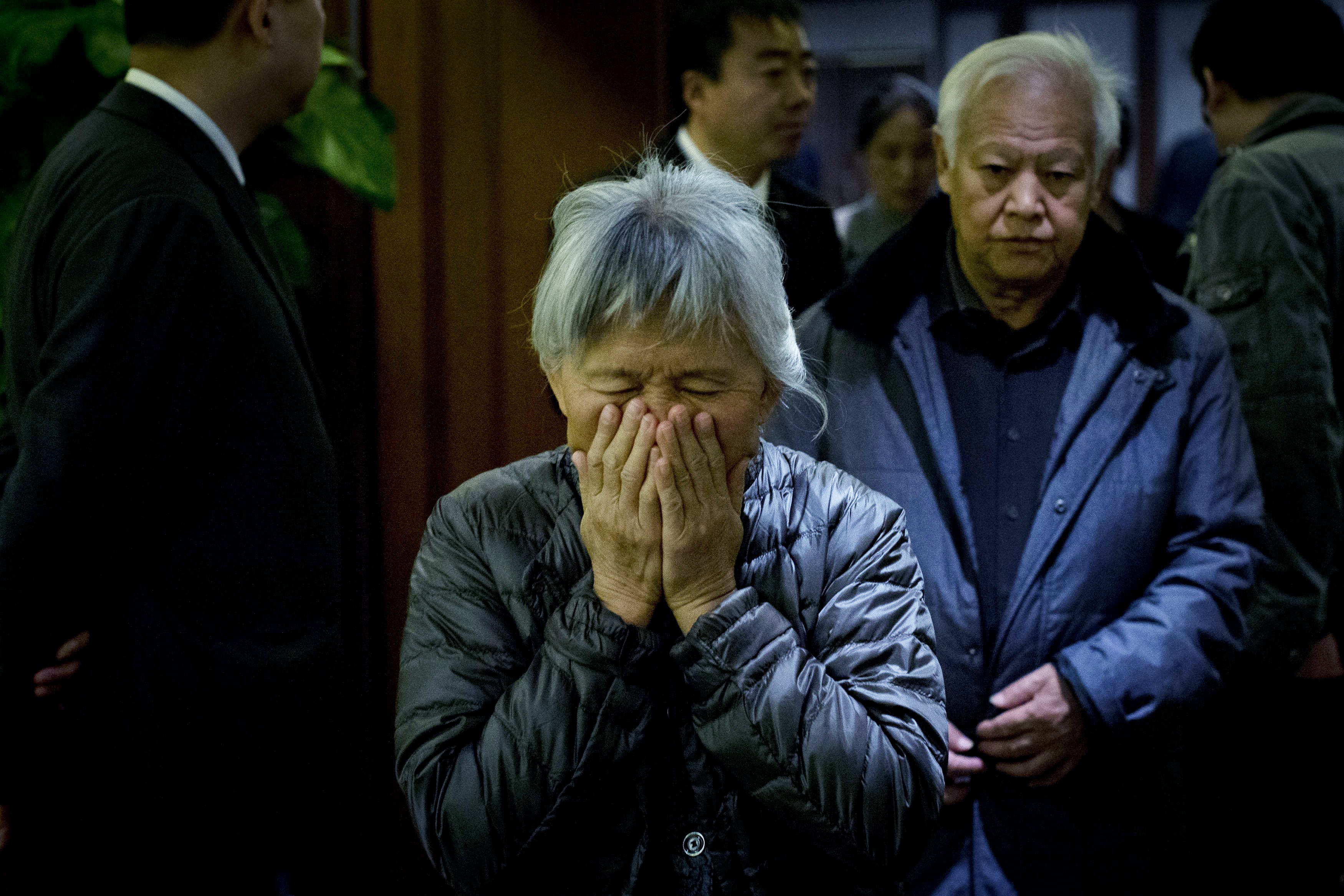 An elderly woman, one of the relatives of Chinese passengers aboard missing Malaysia Airlines Flight MH370, covers her face out of frustration as she leaves a hotel ballroom after a daily briefing meeting with managers of Malaysia Airlines in Beijing, on
