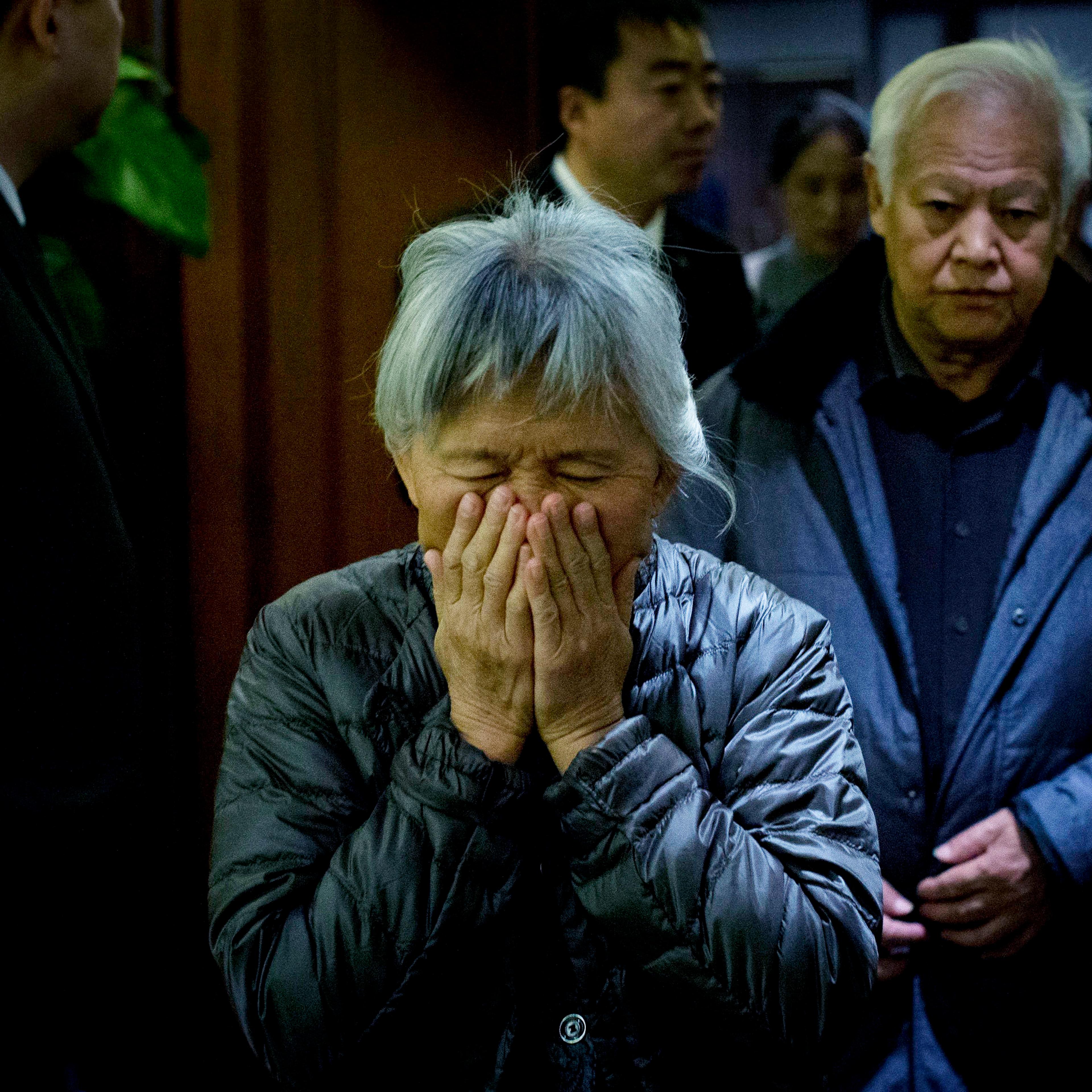 An elderly woman, one of the relatives of Chinese passengers aboard missing Malaysia Airlines Flight MH370, covers her face out of frustration as she leaves a hotel ballroom after a daily briefing meeting with managers of Malaysia Airlines in Beijing, on