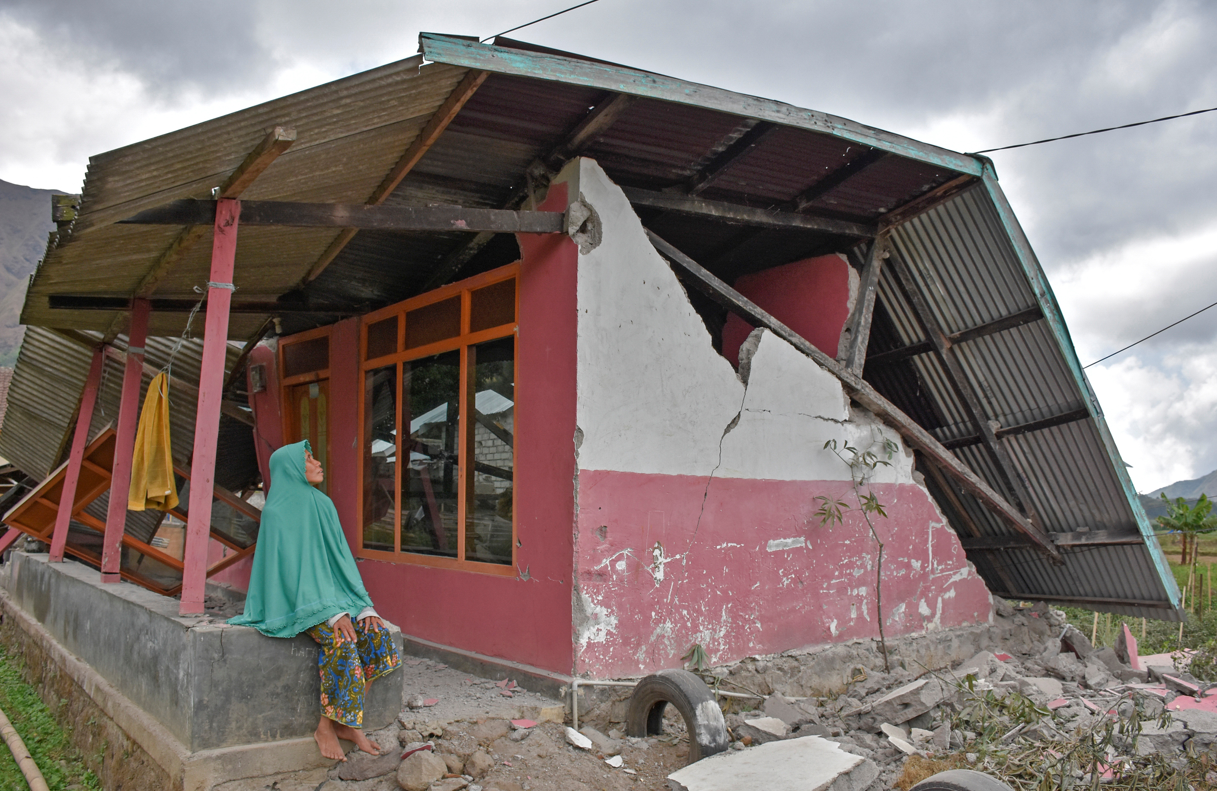 A villager sits at her damaged house after an earthquake hit Sembalun Bumbung village in Lombok Timur