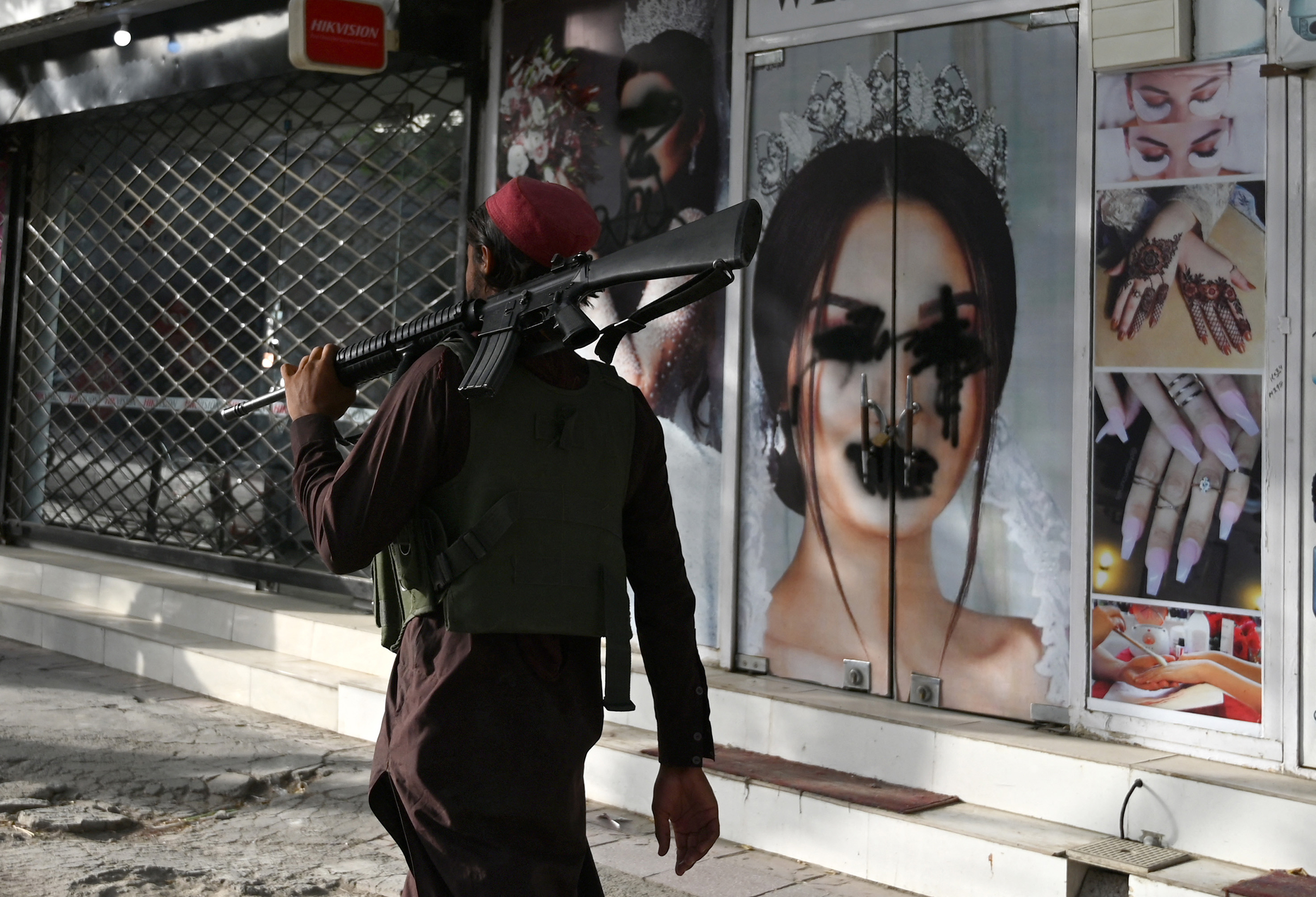 A Taliban fighter walks past a beauty salon with images of women defaced using spray paint in the Shar-e-Naw area of Kabul on Aug. 18, 2021.