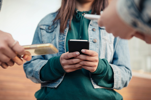 Cropped image of female friends using smart phones outdoors