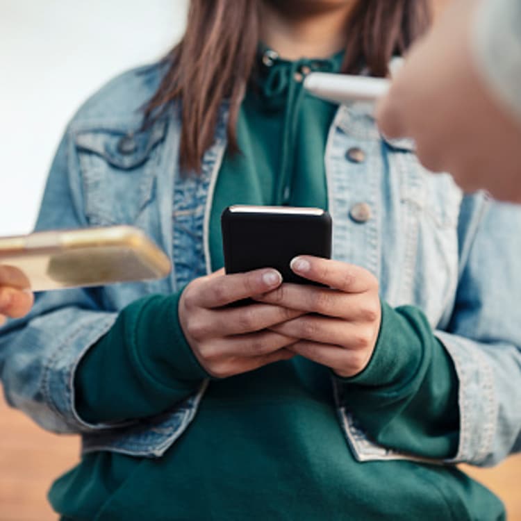 Cropped image of female friends using smart phones outdoors