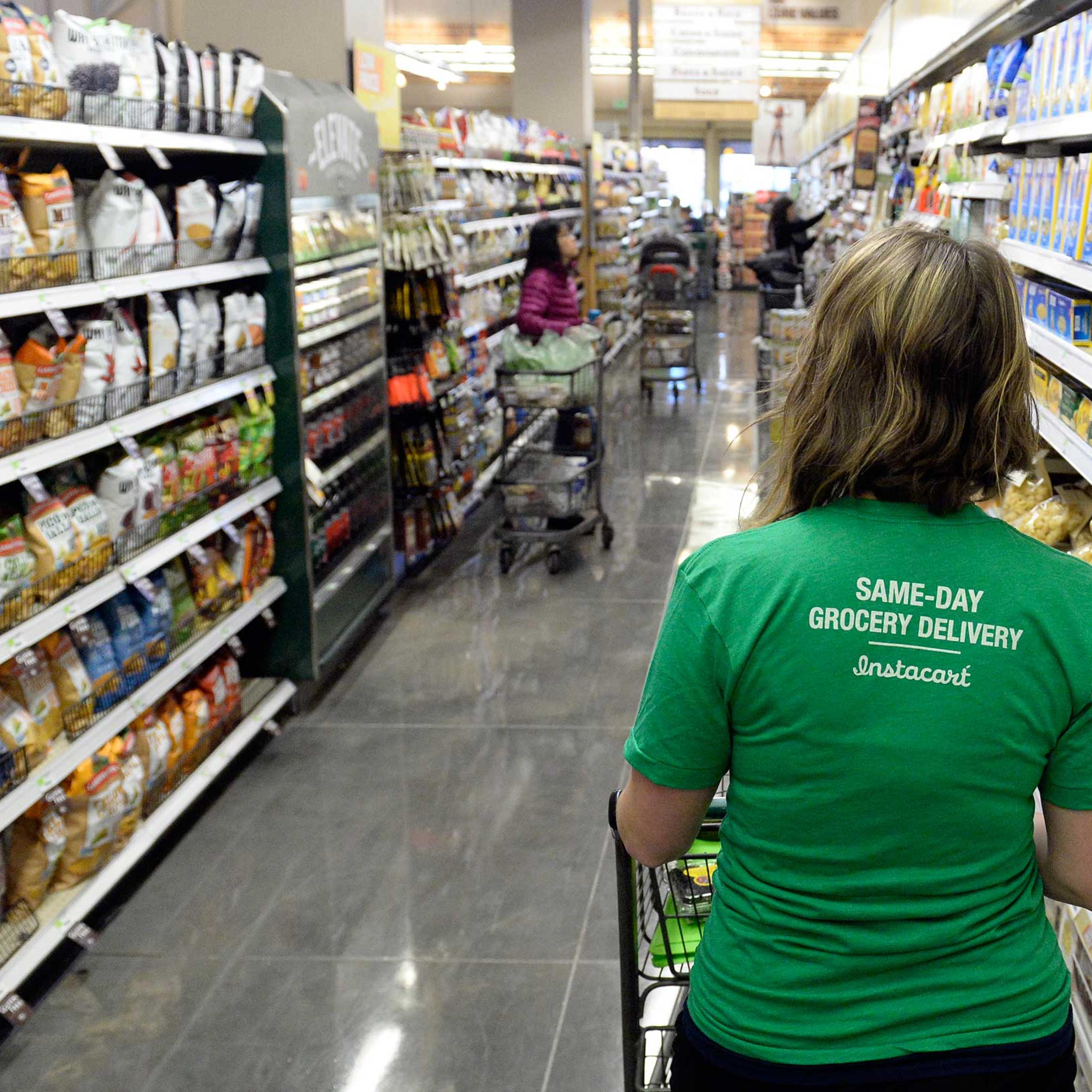 Kaitlin Myers a shopper for Instacart studies her smart phone as she shops for a customer at Whole Foods in Denver.