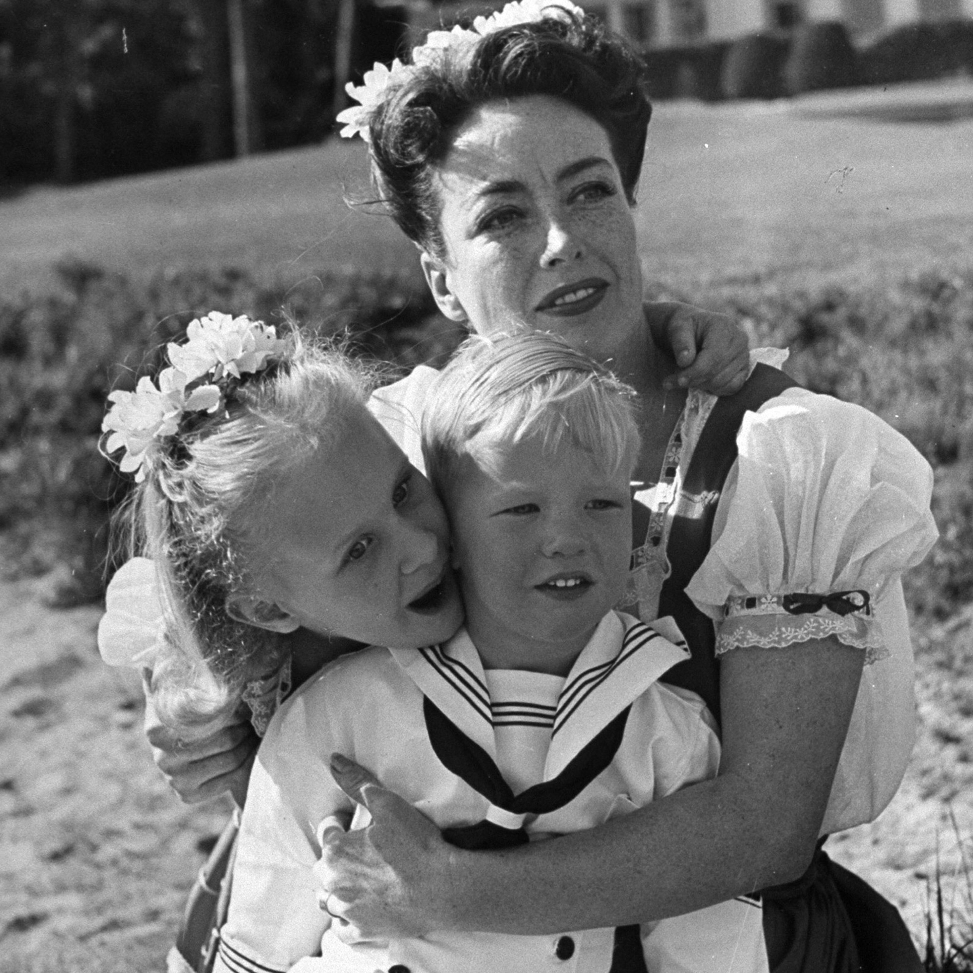 Joan Crawford hugging her two adopted children, Christina and Christopher, while sitting on beach, 1945.