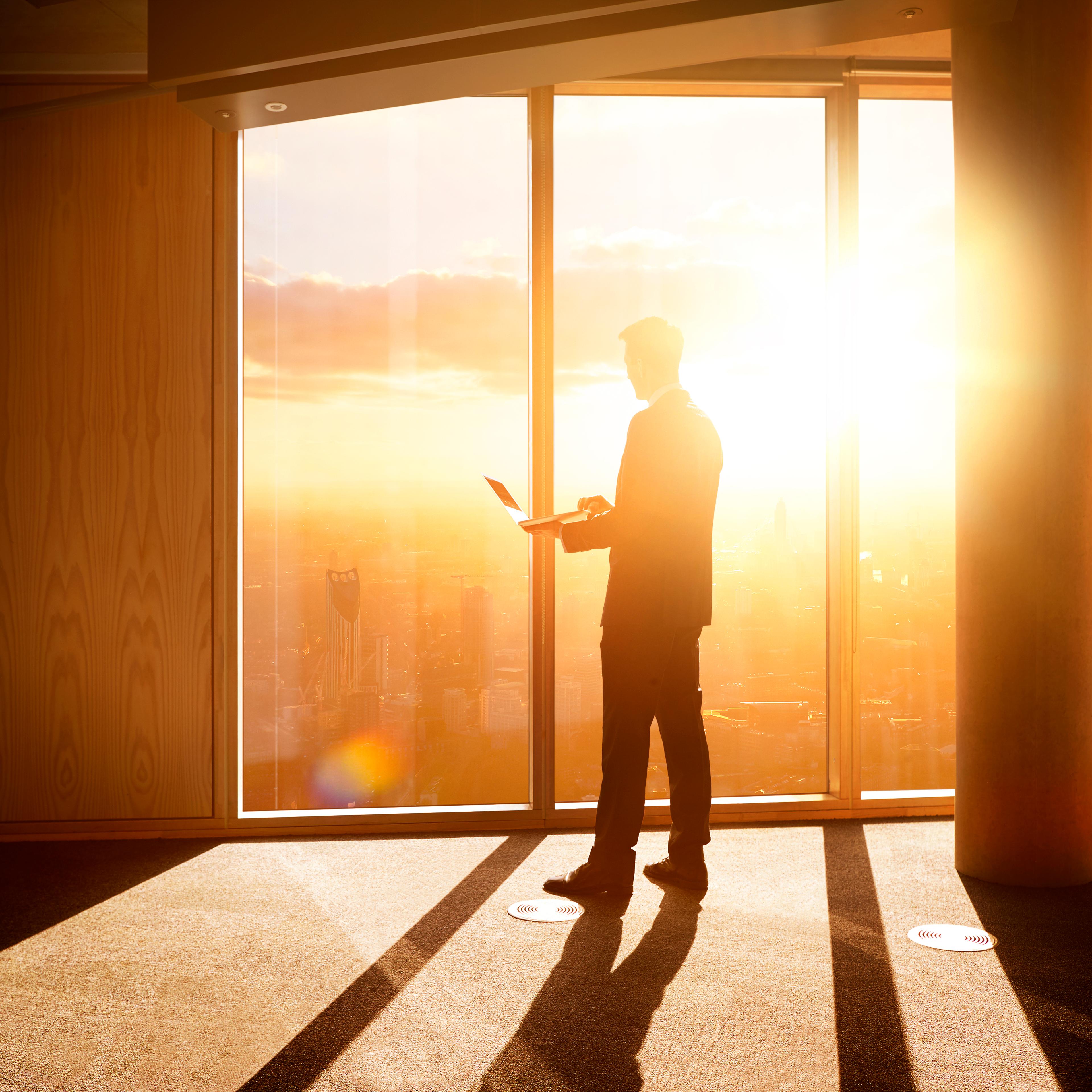 Businessman looking out over the city at sunrise.