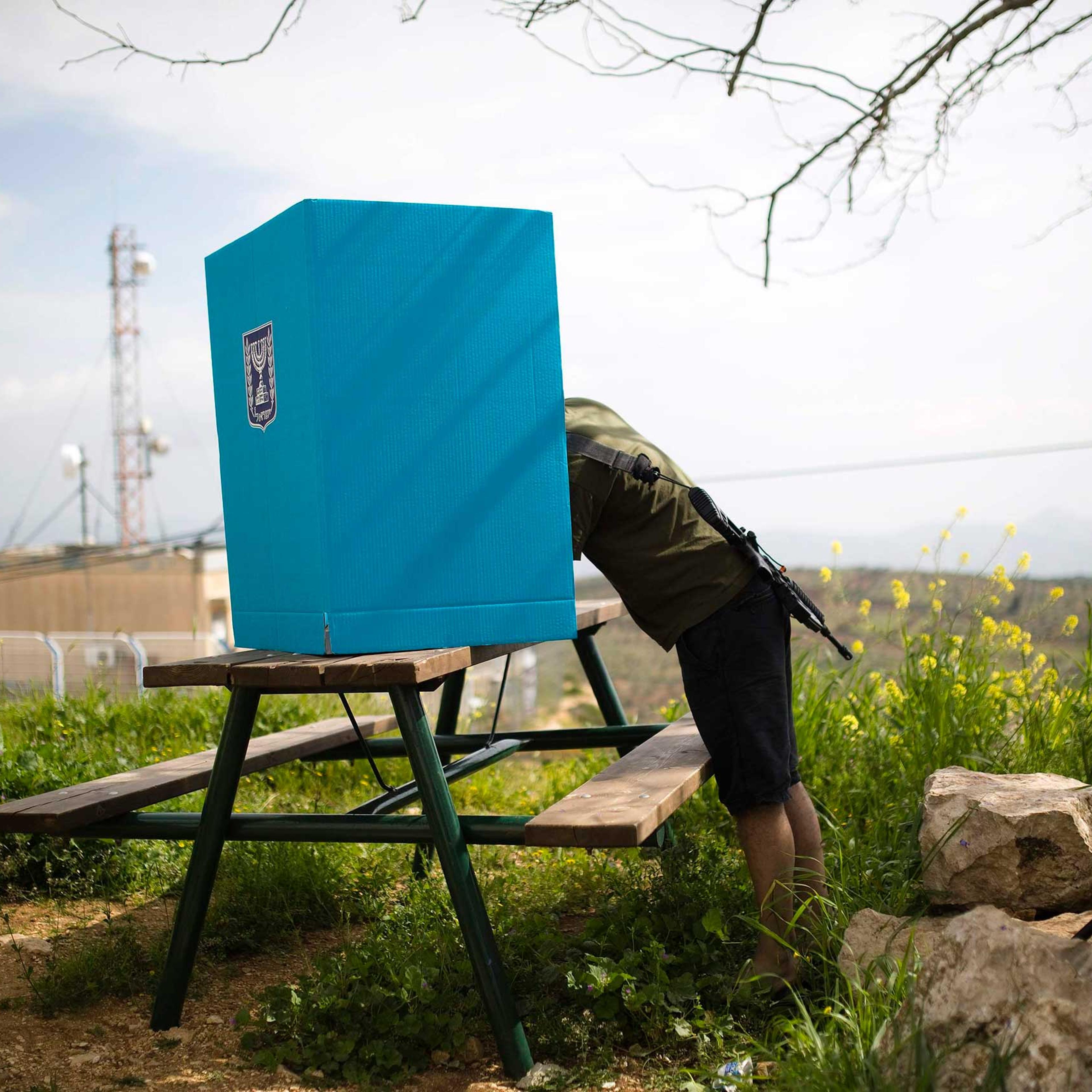 An Israeli soldier casts his ballot for the parliamentary election behind a mobile voting booth in the West Bank Jewish settlement of Migdalim, near Ariel, March 17, 2015.