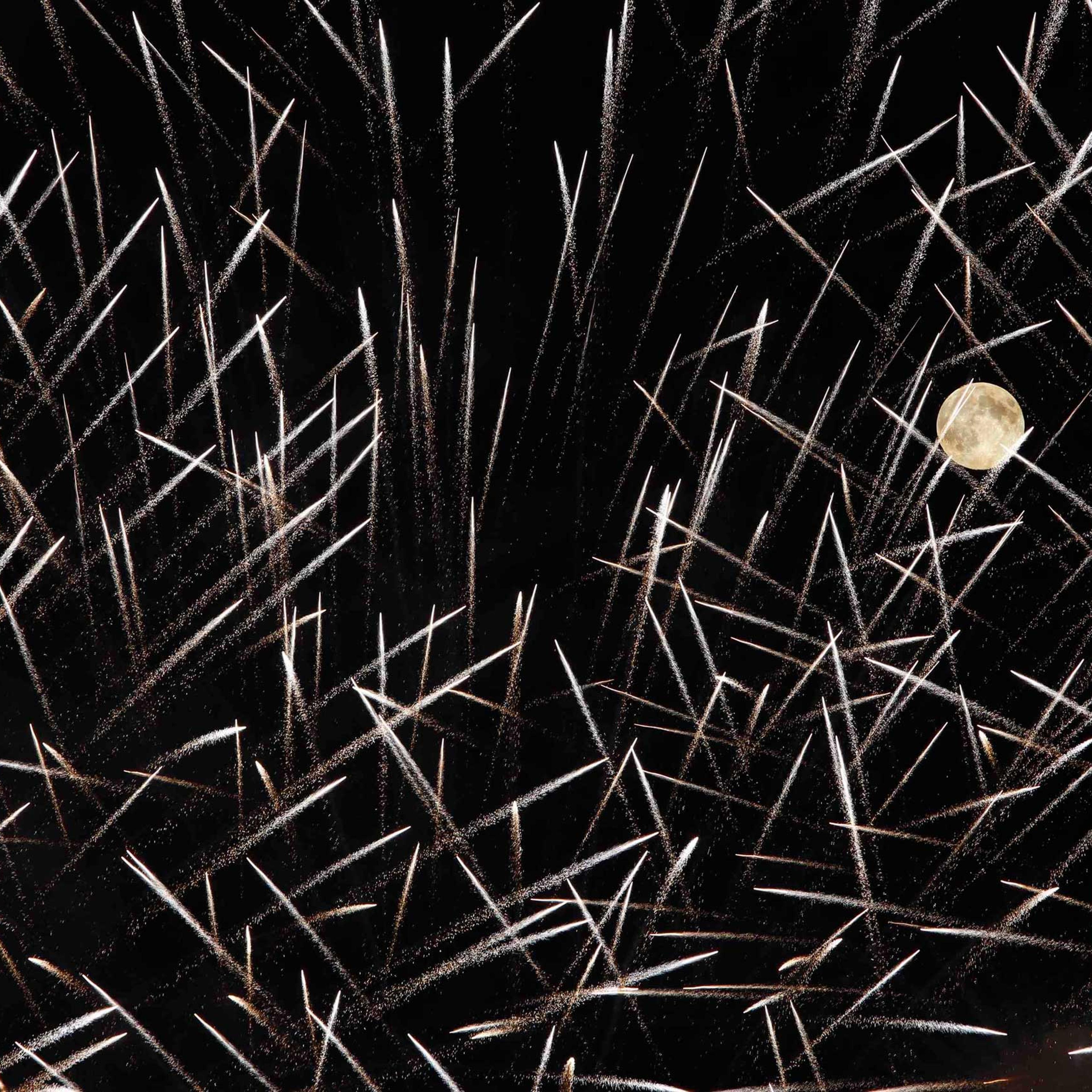 Fireworks streak past in front of the supermoon outside the town of Mosta
