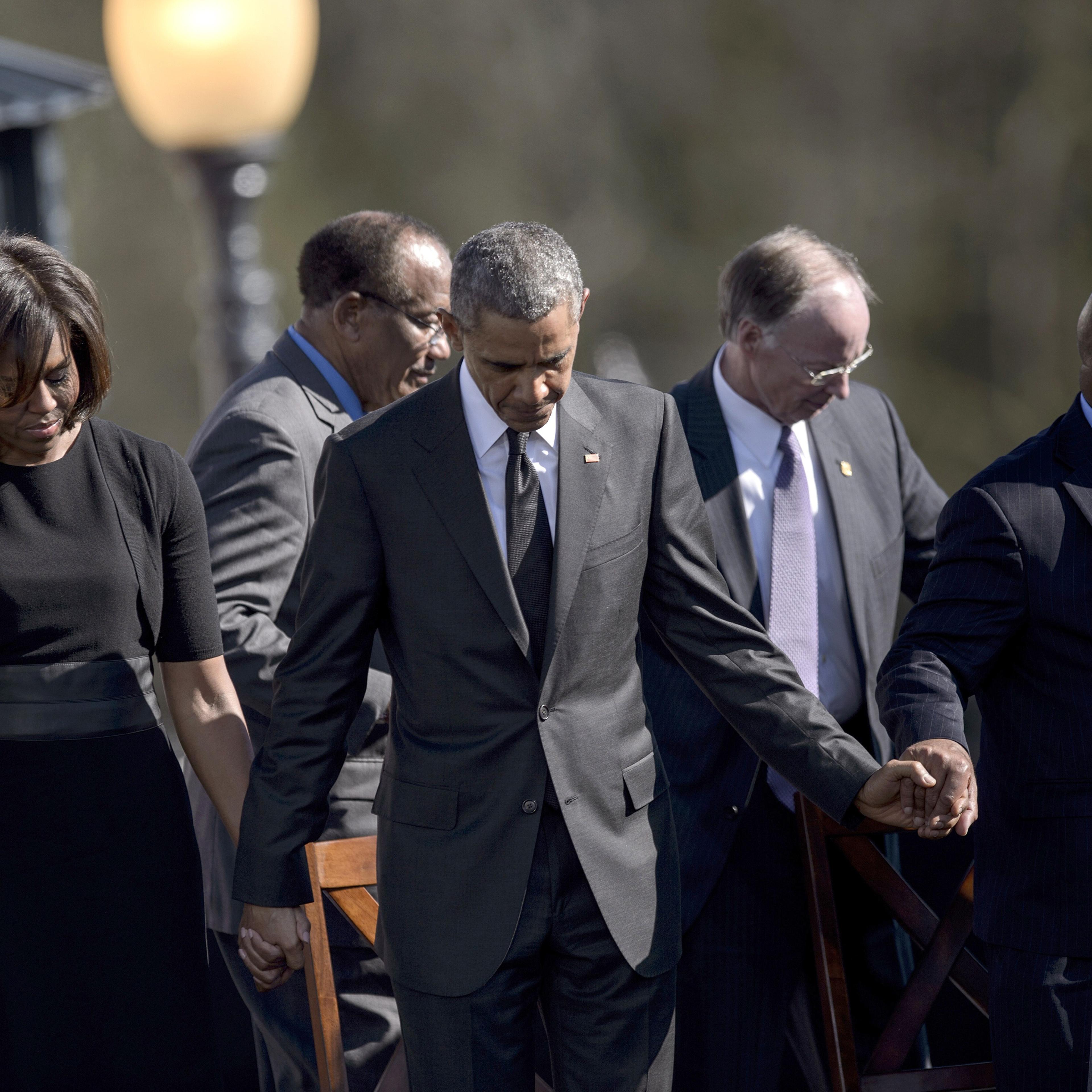 (L-R) US First Lady Michelle Obama, US President Barack Obama, Robert J. Bentley and US Representative John Lewis bow their heads for a prayer at the Edmund Pettus Bridge on March 7, 2015 in Selma, Alabama. Obama marked the 50th anniversary of the Selma