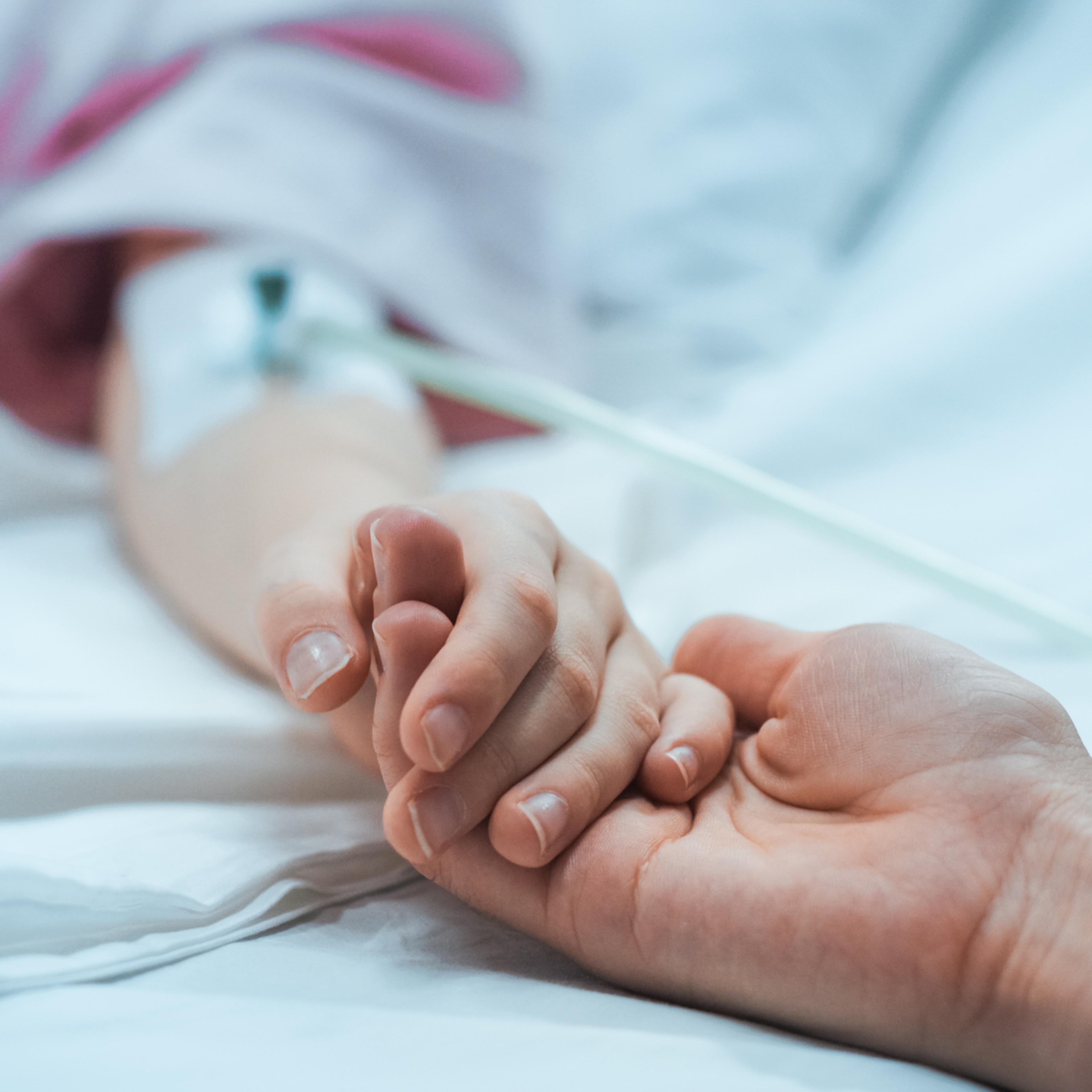 Recovering Little Child Lying in the Hospital Bed Sleeping, Mother Holds Her Hand Comforting. Focus on the Hands. Emotional Family Moment.