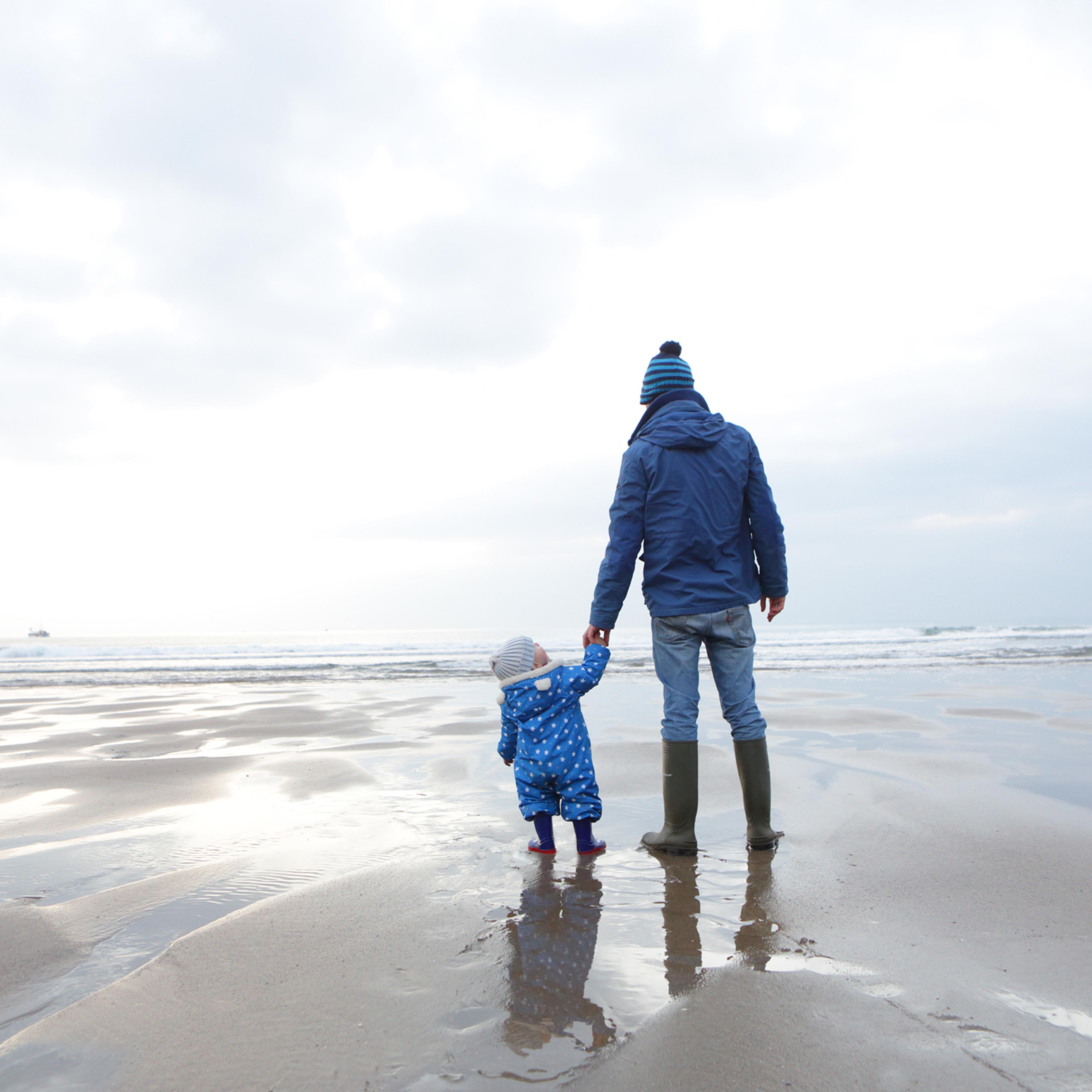father and child on the beach , child looks up .