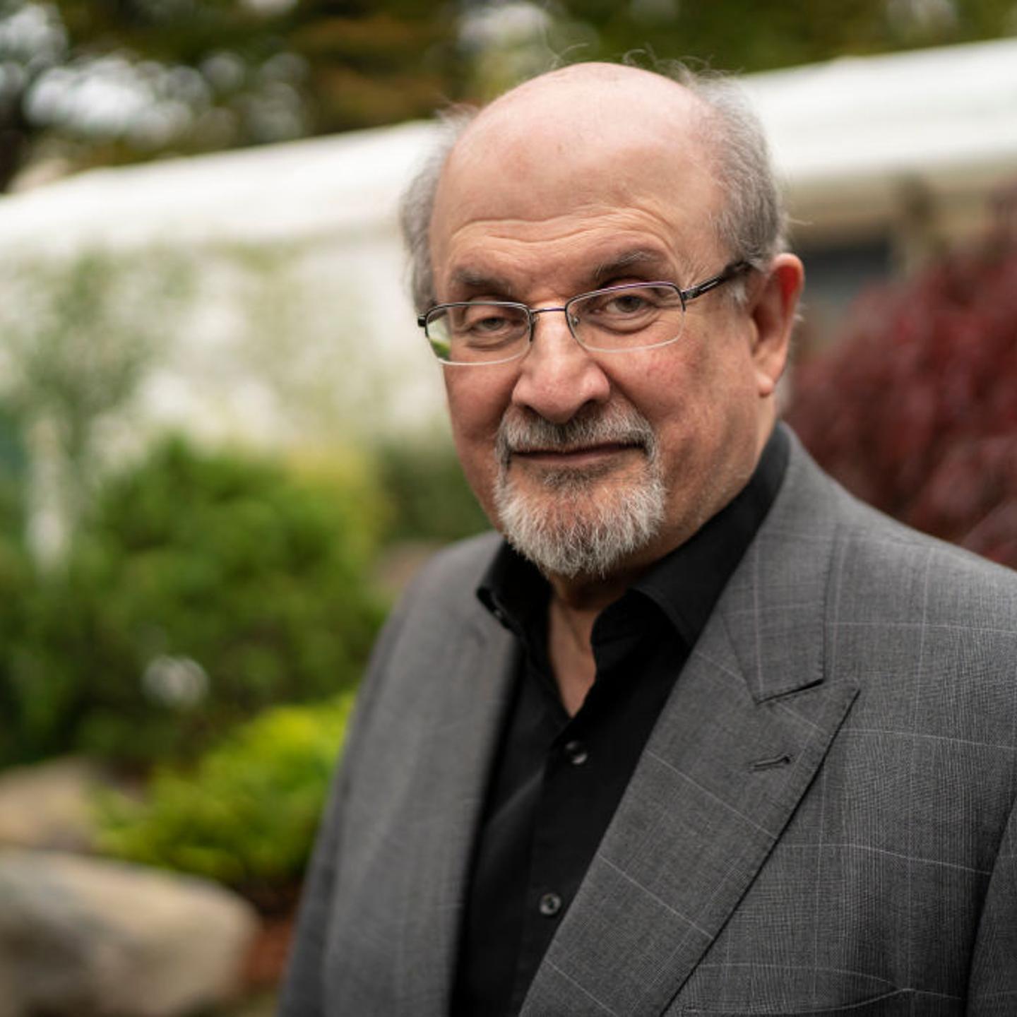 Salman Rushdie smiles gently at the camera in a gray suit
