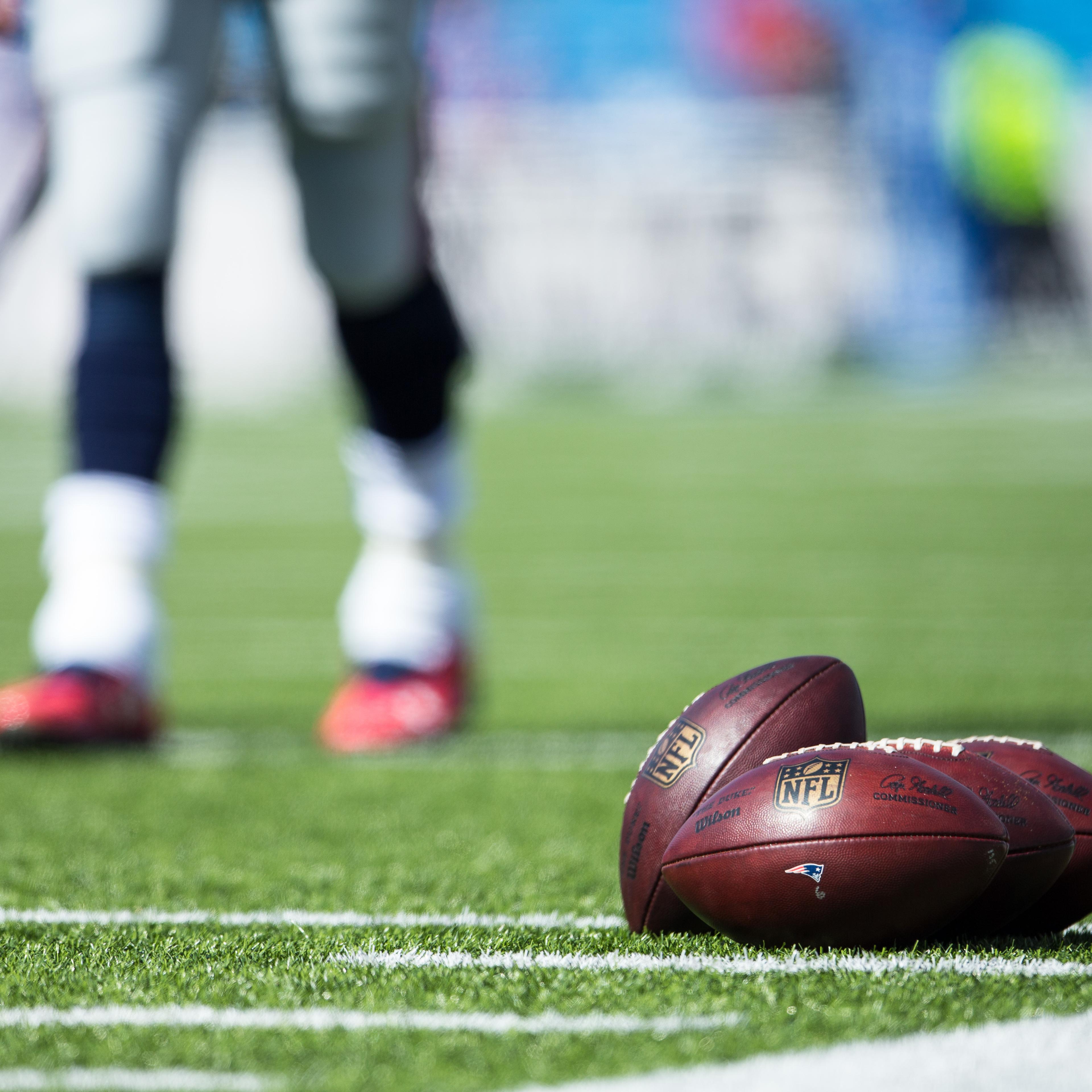 ORCHARD PARK, NY - SEPTEMBER 20: Wilson NFL Footballs bearing the New England Patriots logo set on the turf as Tom Brady #12 warms up in the background before the game against the Buffalo Bills on September 20, 2015 at Ralph Wilson Stadium in Orchard Pa