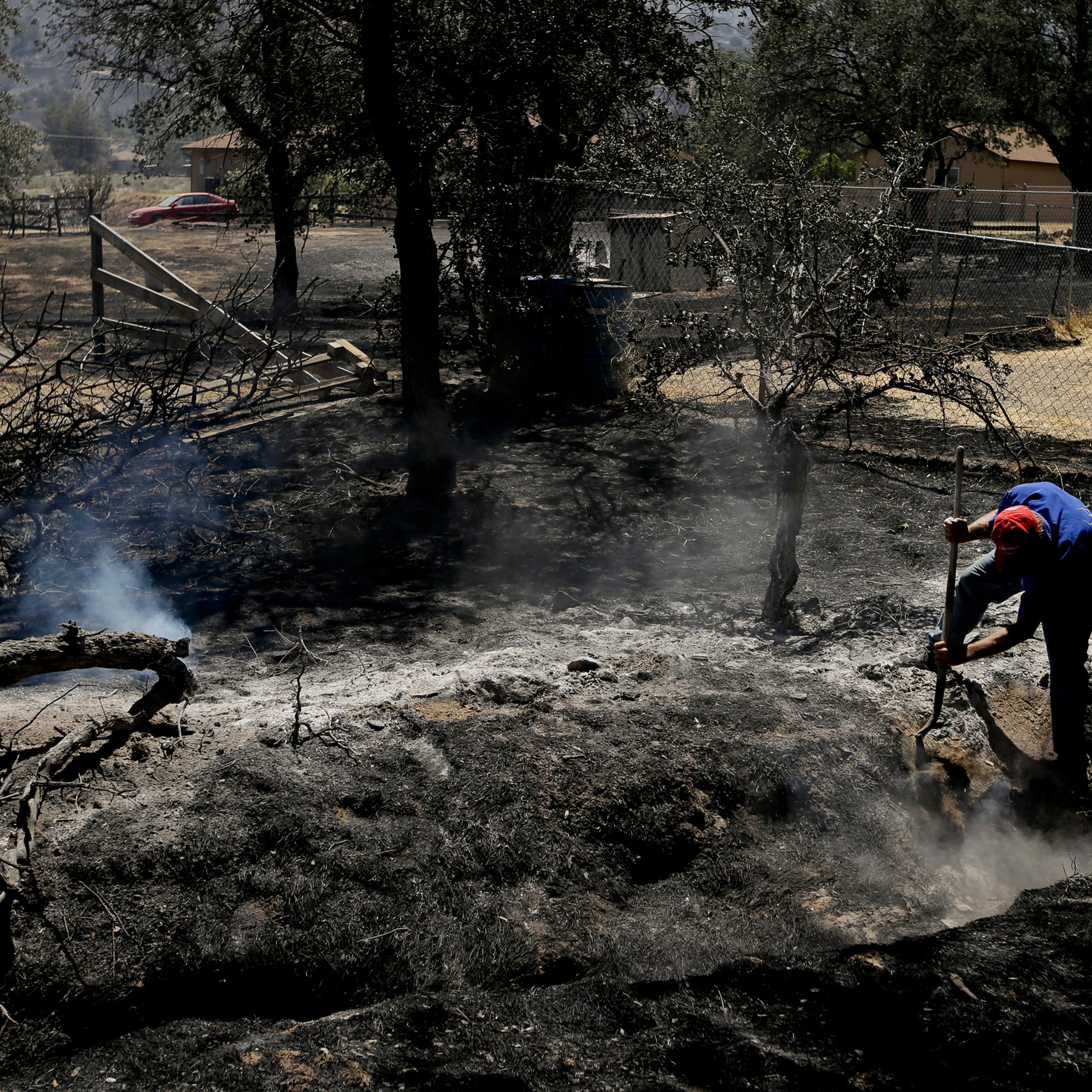 Alan Germain puts out hotspots on his neighbor's property destroyed by a wildfire Friday, June 24, 2016, near Lake Isabella, Calif. The wildfire that roared across dry brush and trees in the mountains of central California gave residents little time to f