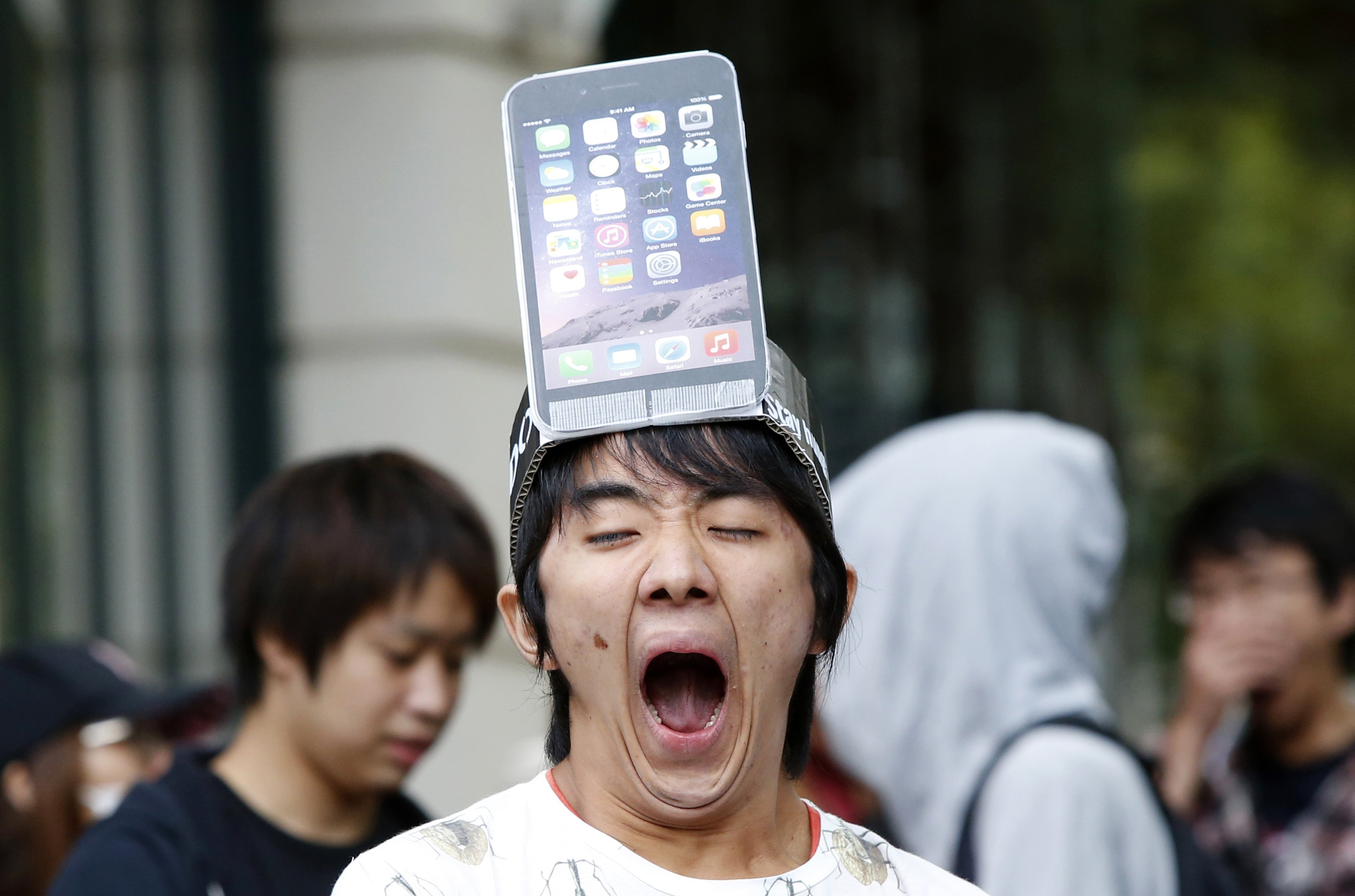 A man wearing a replica of an iPhone 6 Plus model on his head yawns while waiting in front of the Apple Store in Tokyo on Sept. 19, 2014.