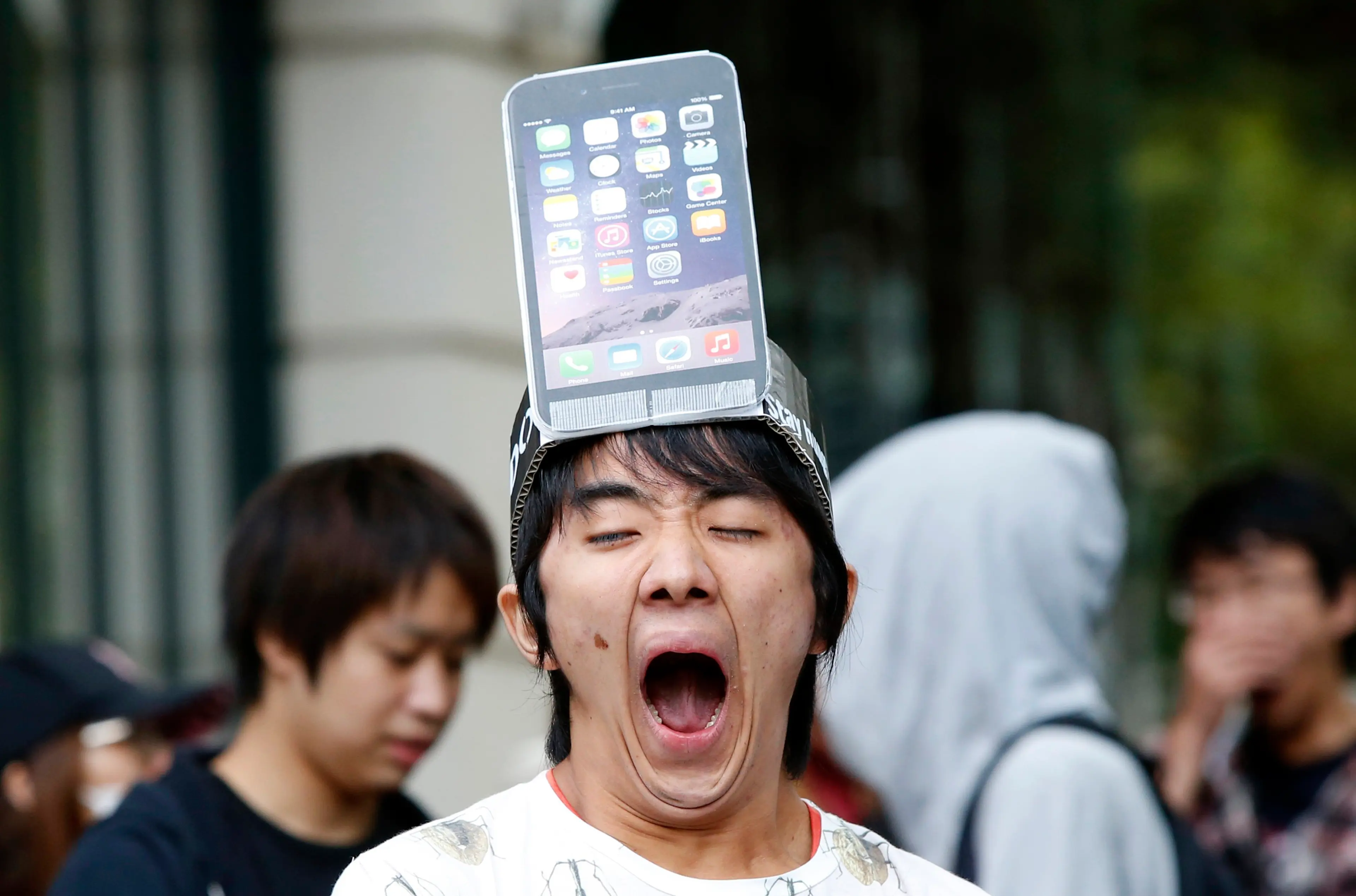 A man wearing a replica of an iPhone 6 Plus model on his head yawns while waiting in front of the Apple Store in Tokyo on Sept. 19, 2014.