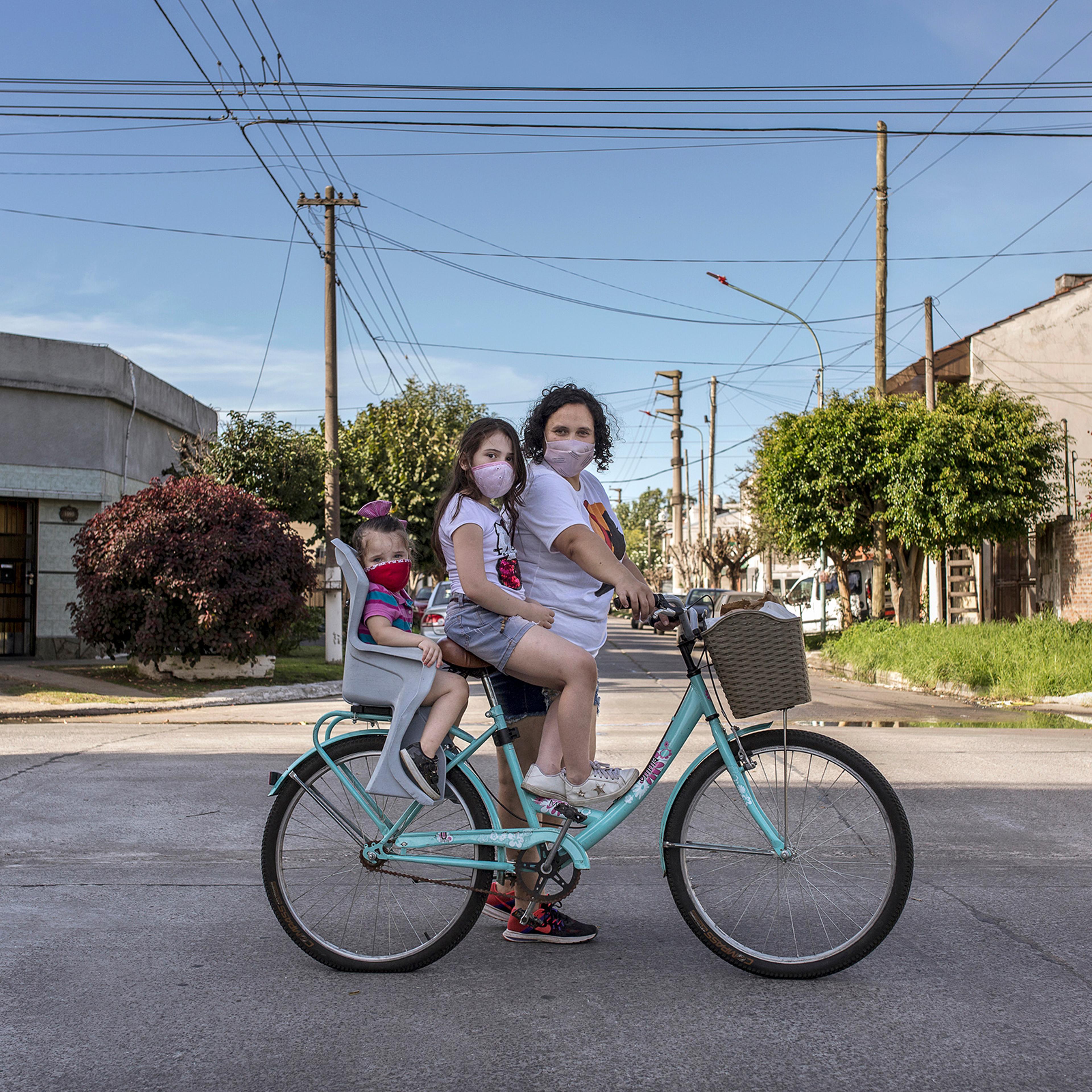María Teresa Arzamendia stands for a portrait with her two daughters Leia and Catalina and her bicycle with pastries in El Palomar, Buenos Aires Province, on April 17.
