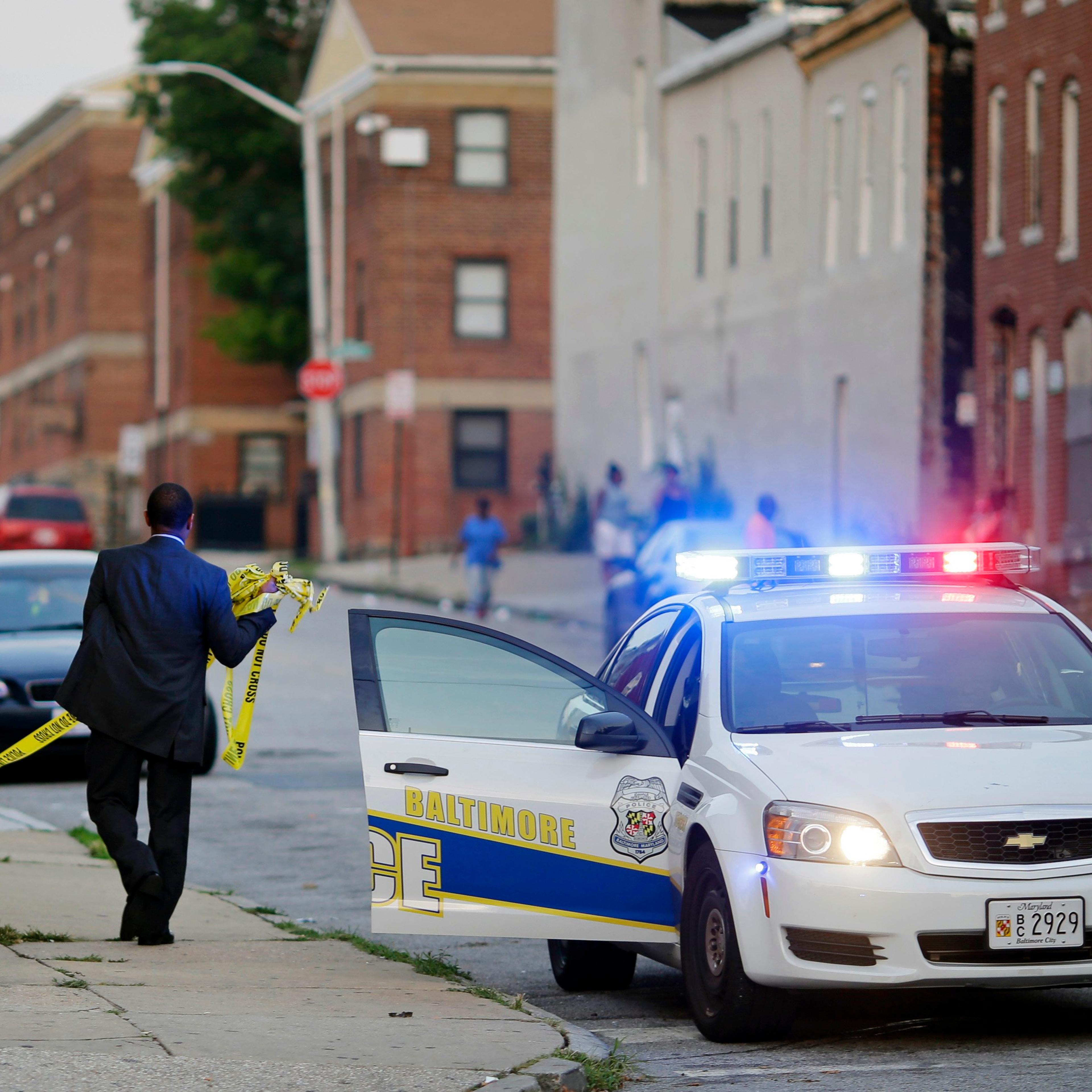 A member of the Baltimore Police Department removes crime scene tape from a corner where a victim of a shooting was discovered in Baltimore on July 30, 2015.