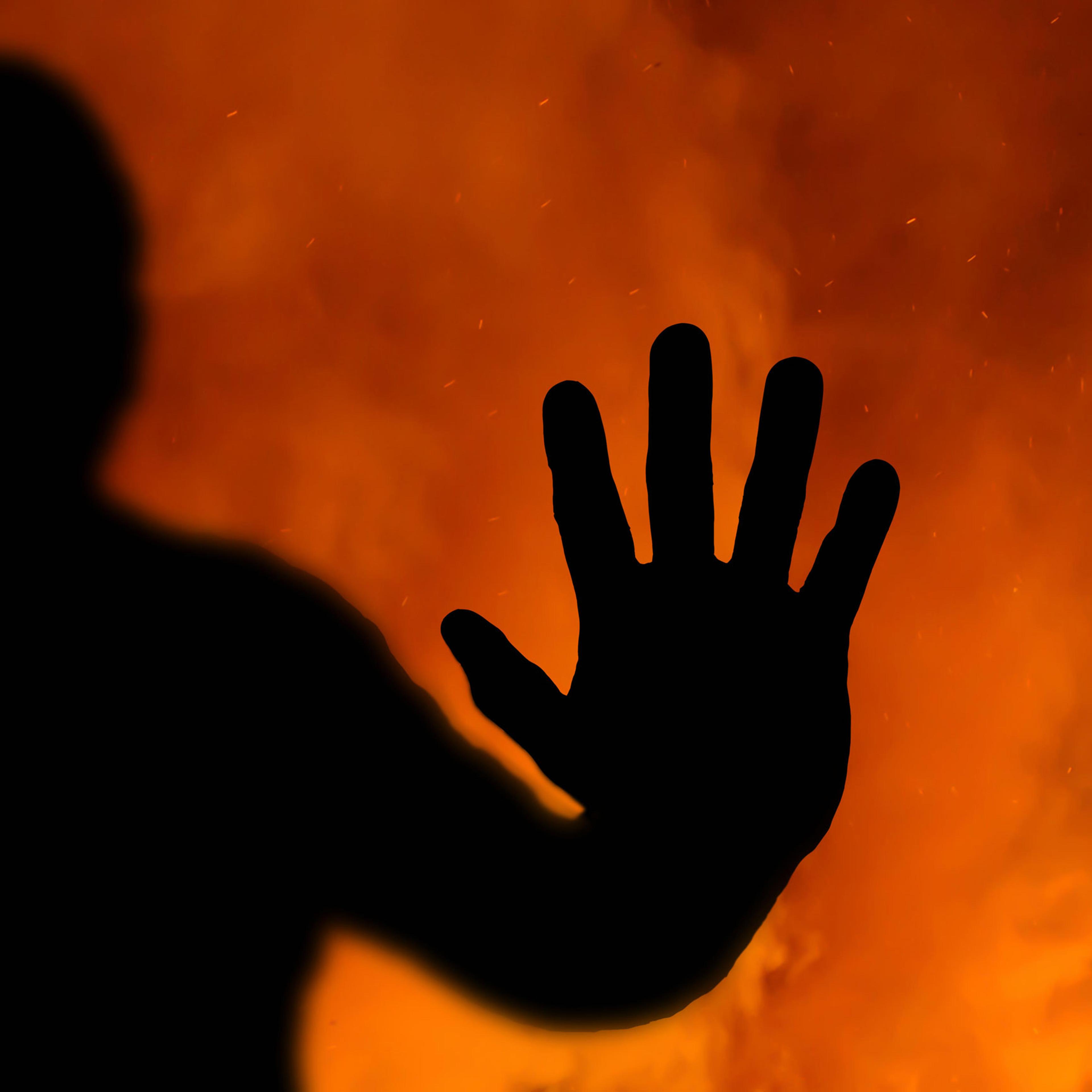 Abstract of a silhouette of the hand pressed up against the inside of a window with a fire raging in the background