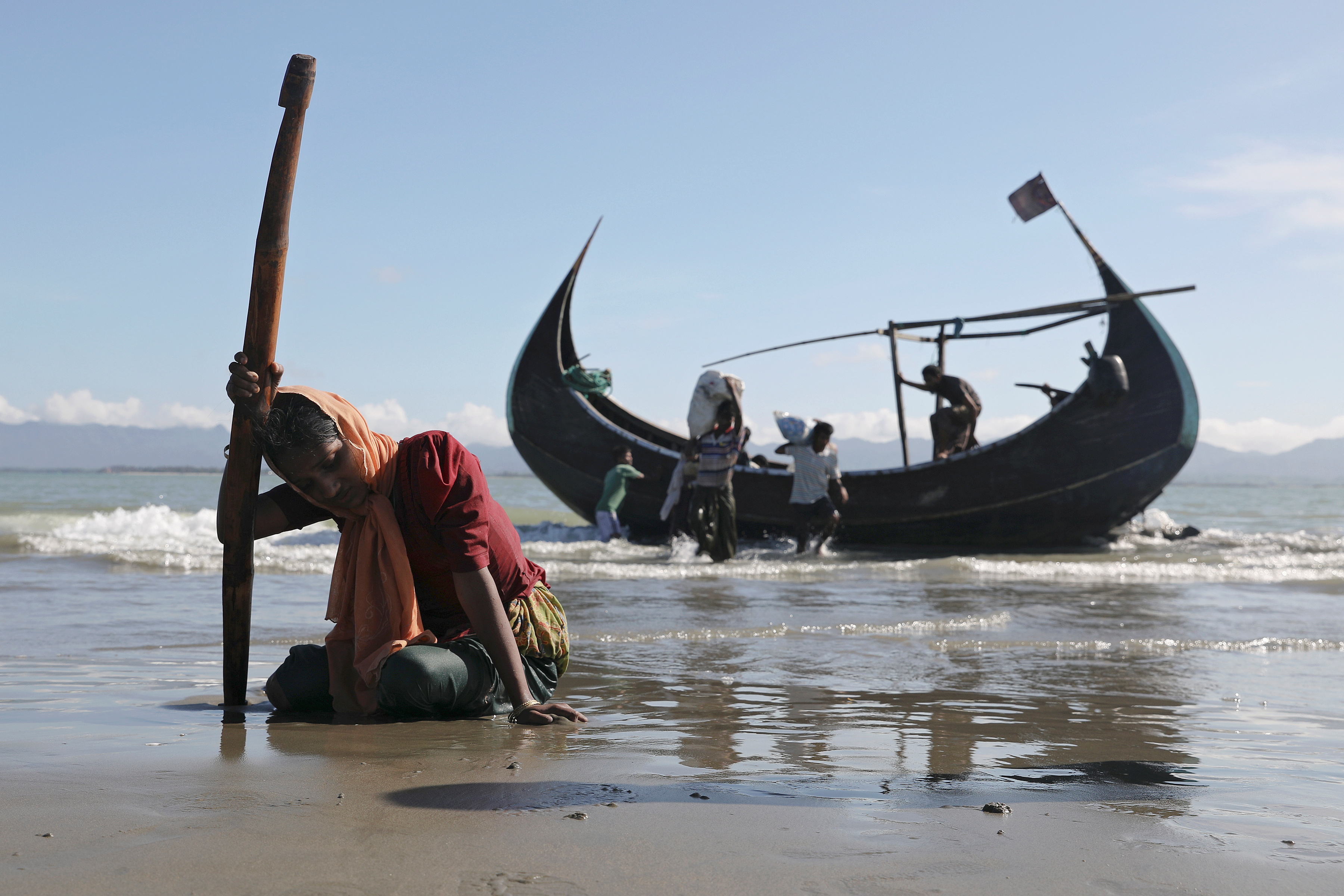 A woman collapses from exhaustion as Rohingya refugees arrive by a wooden boat from Myanmar to the shore of Shah Porir Dwip