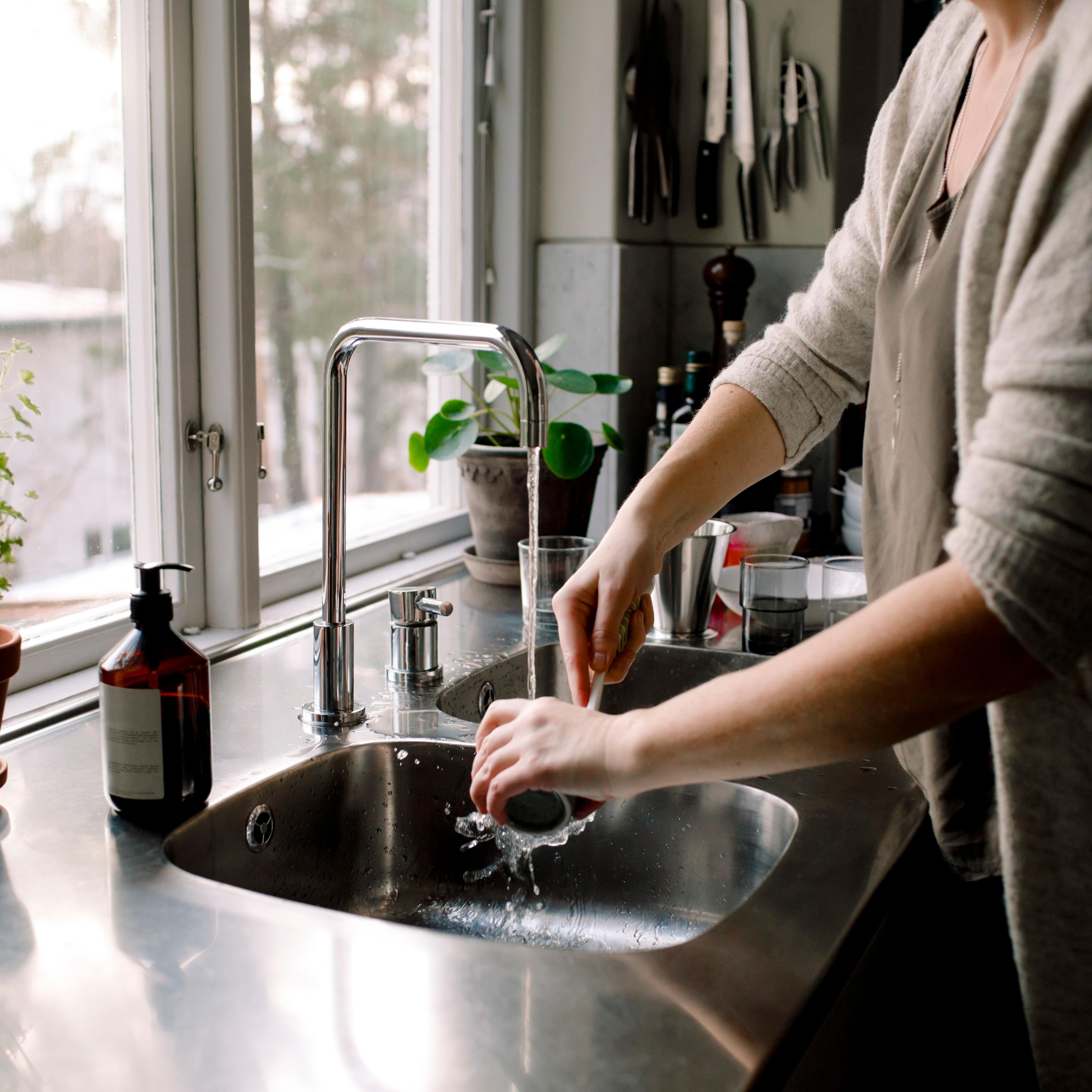 A woman cleans a cup in the kitchen sink at home