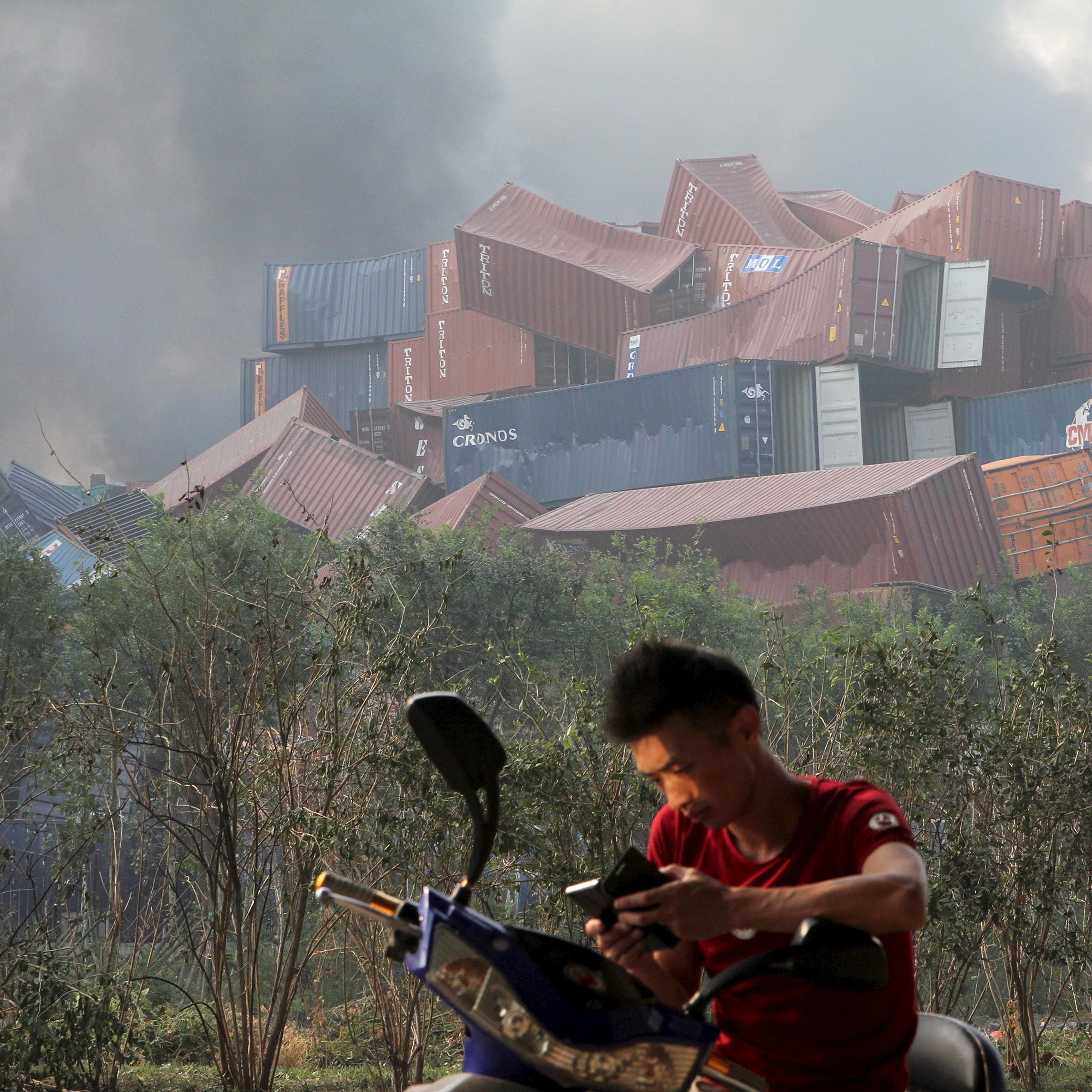 A man checks his mobile phone near overturned shipping containers after explosions in Tianjin