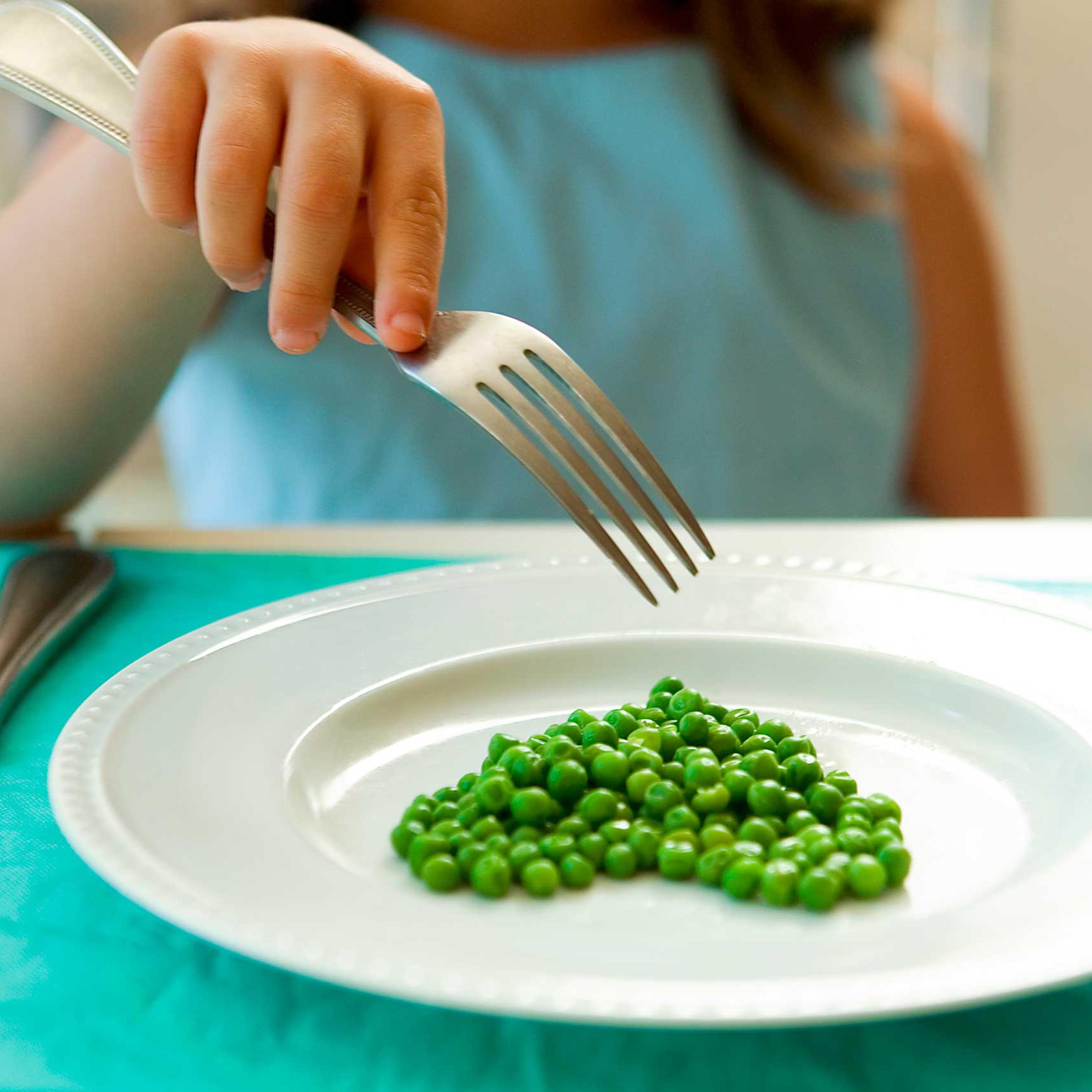 Girl eating green peas with a fork