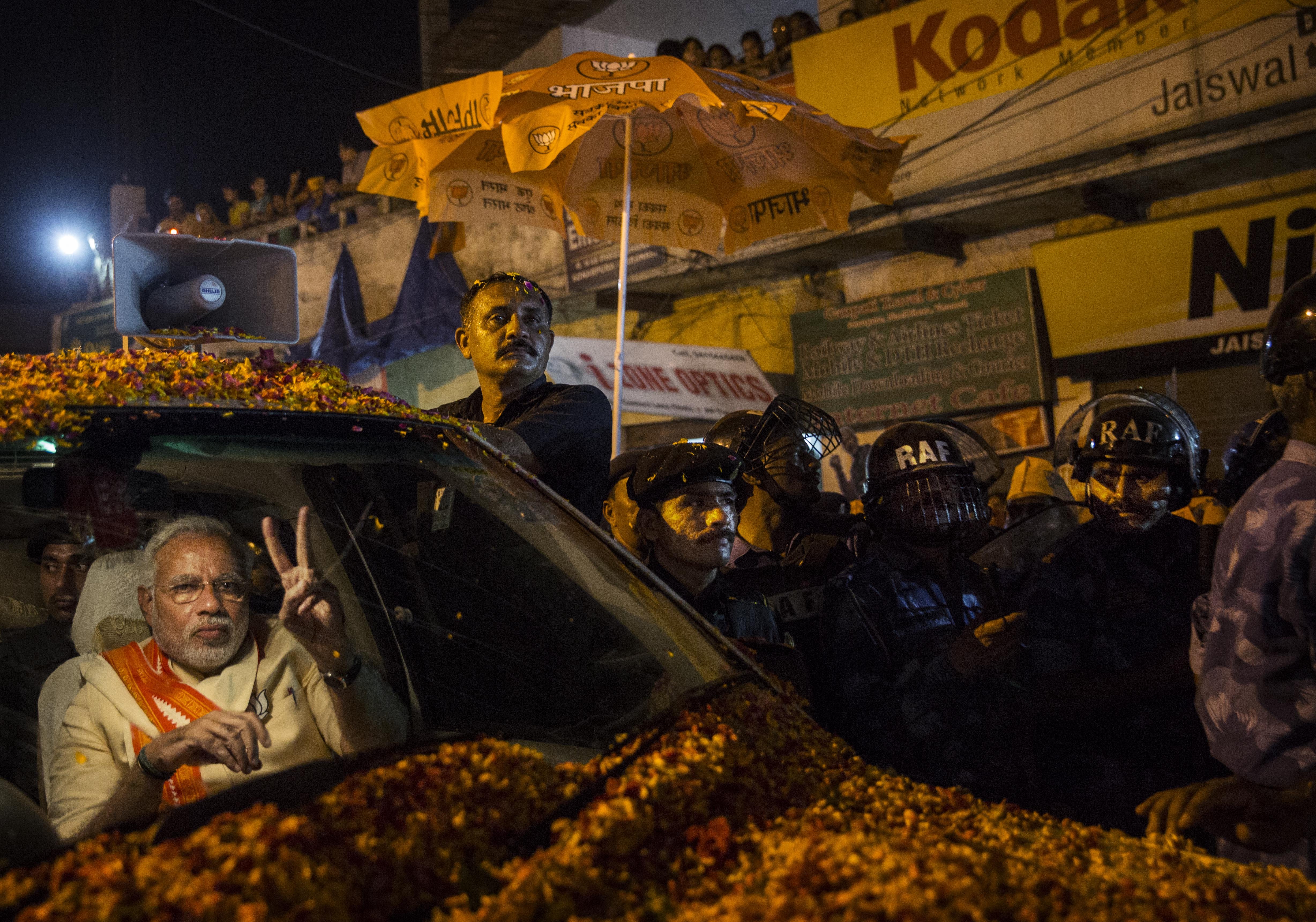 BJP leader Narendra Modi flashes the v-sign to supporters as he is surrounded by bodyguards while driving through the streets on May 8, 2014 in Varanasi, India.