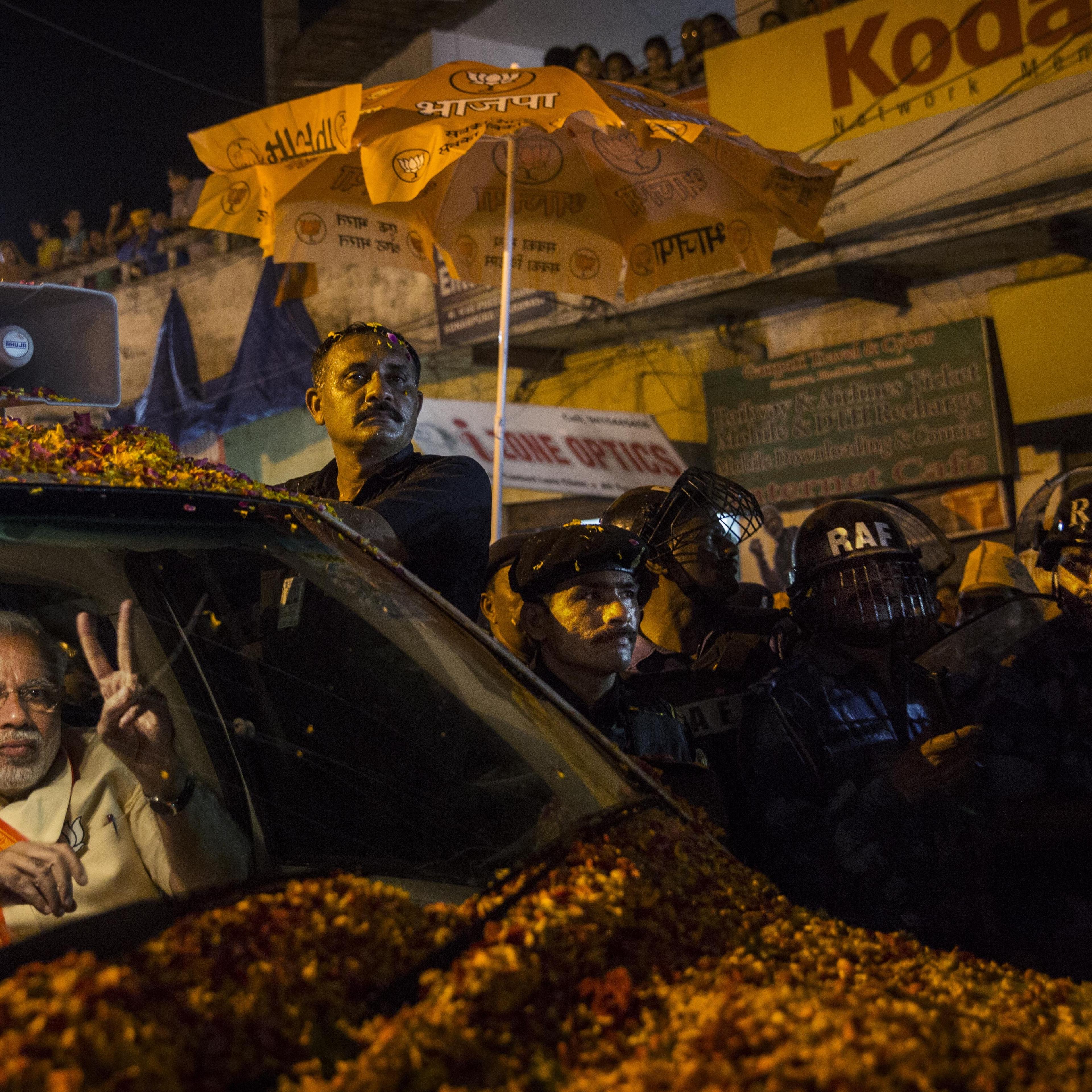 BJP leader Narendra Modi flashes the v-sign to supporters as he is surrounded by bodyguards while driving through the streets on May 8, 2014 in Varanasi, India.