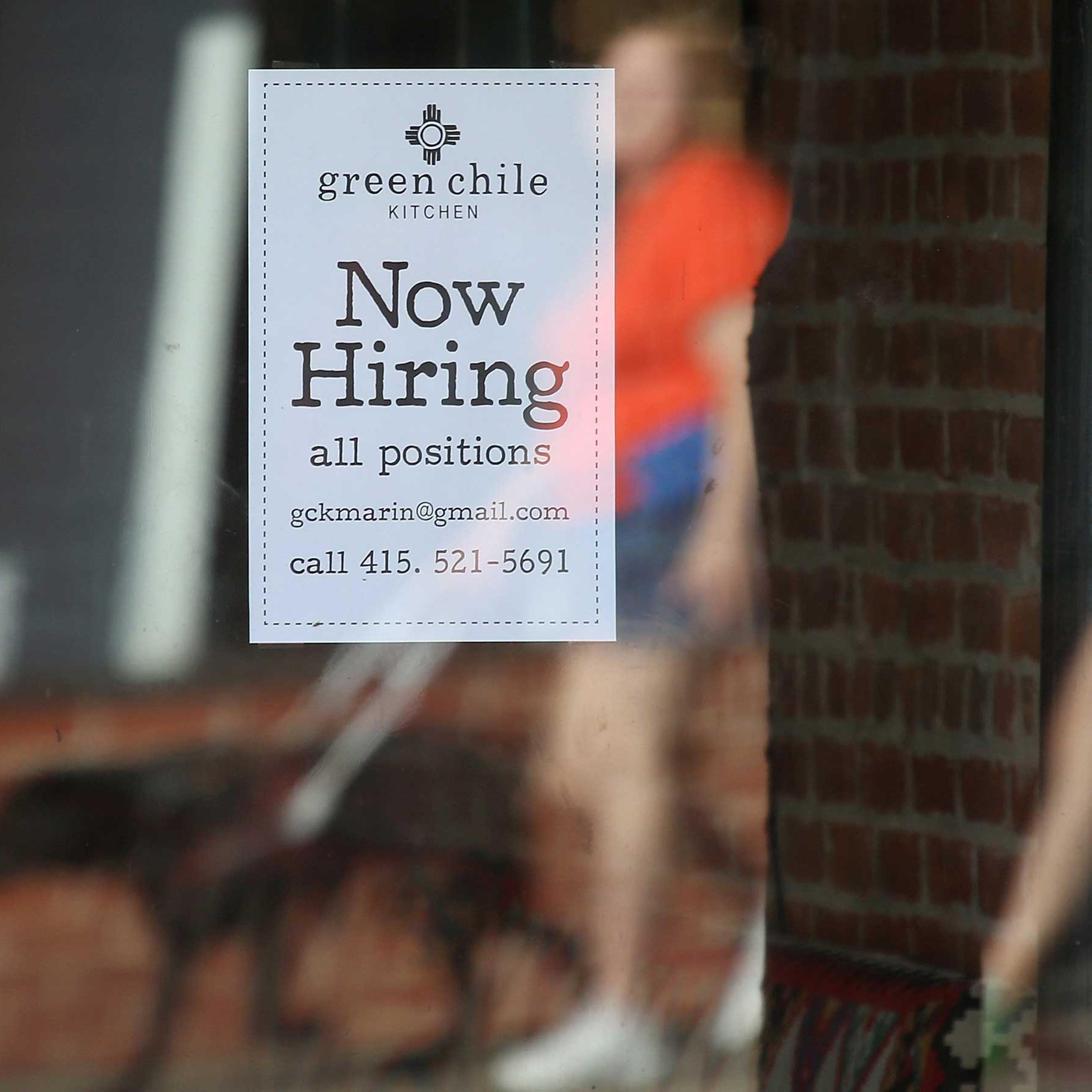 Pedestrians walk by a now hiring sign posted in the window of a business on Nov. 7, 2014 in San Rafael, Calif.