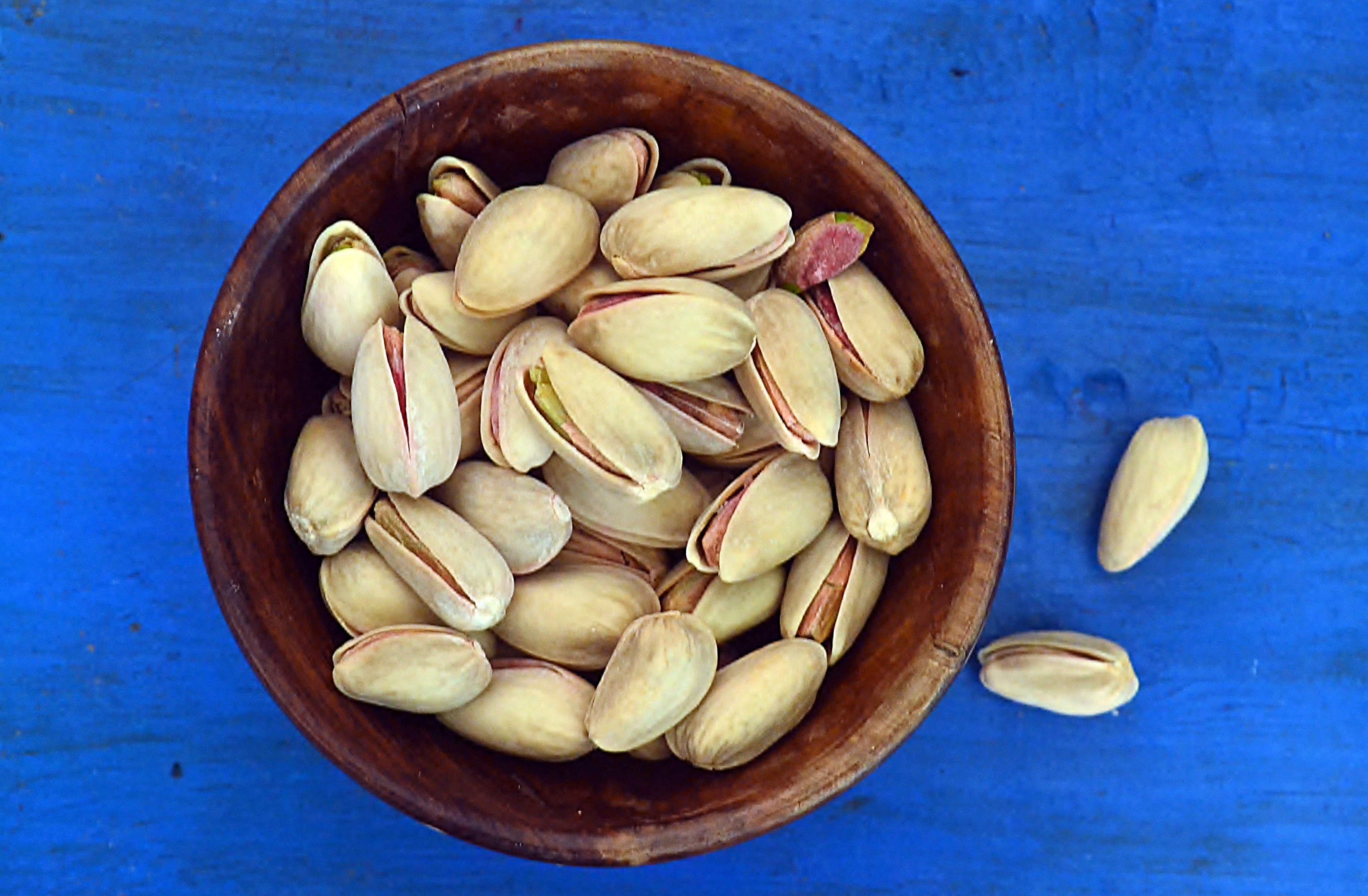 Pistachio nuts in a wooden bowl against blue background